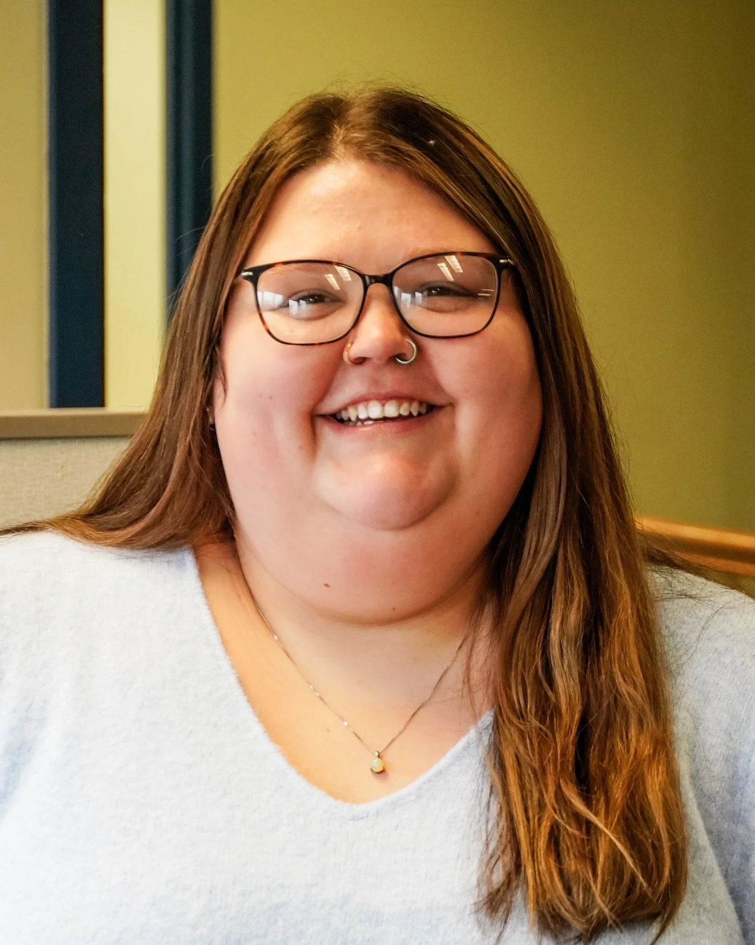Kaitlynn May wears glasses while smiling inside the BBBS office