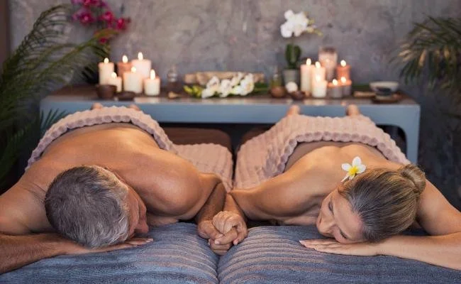 Couple receiving side-by-side massages in a candlelit spa setting.