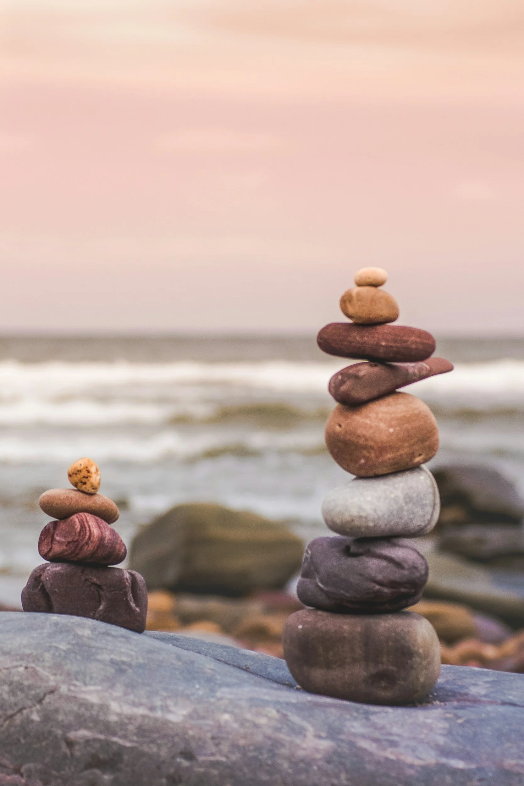 Balanced stones on a beach beneath a soft pink sky.