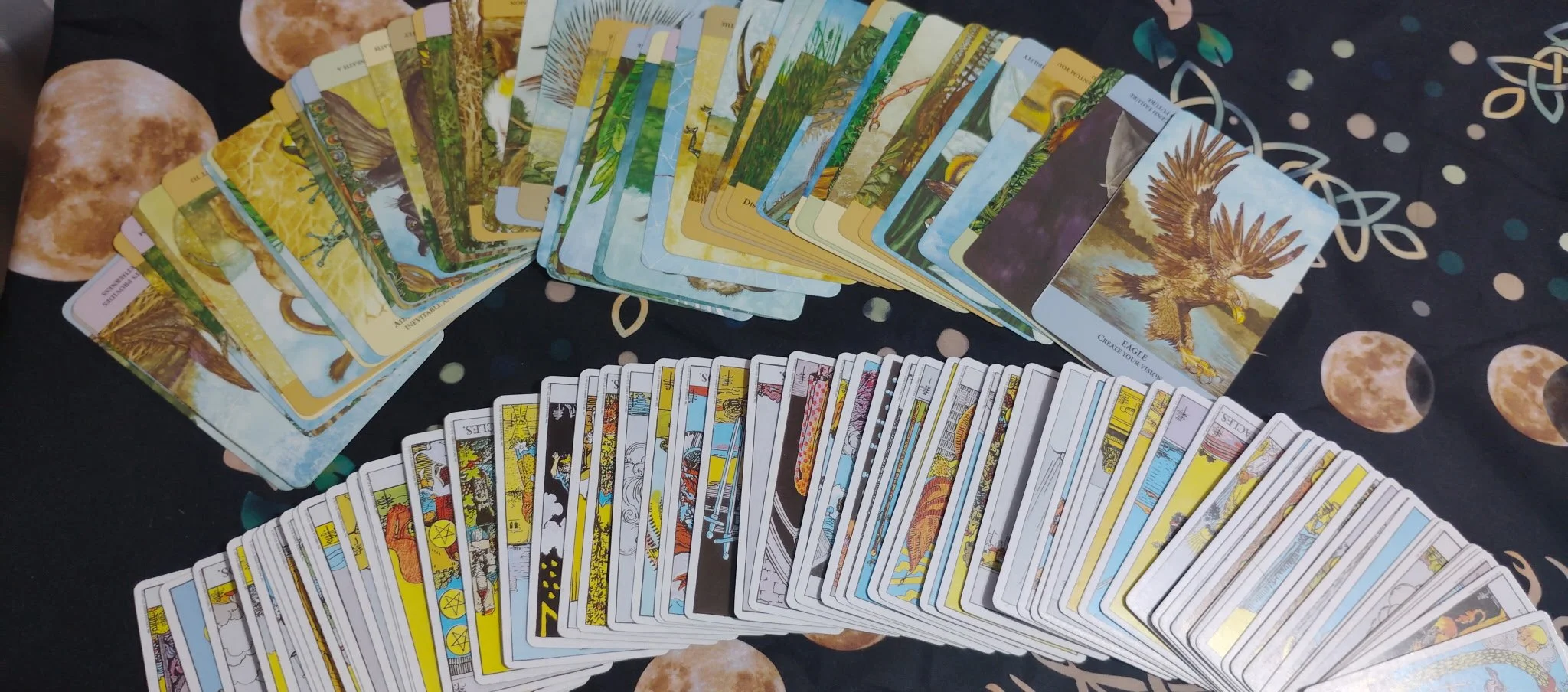 A spread of tarot cards arranged on a space-themed cloth with moons and planets, displaying numerous cards from the Major and Minor Arcana.