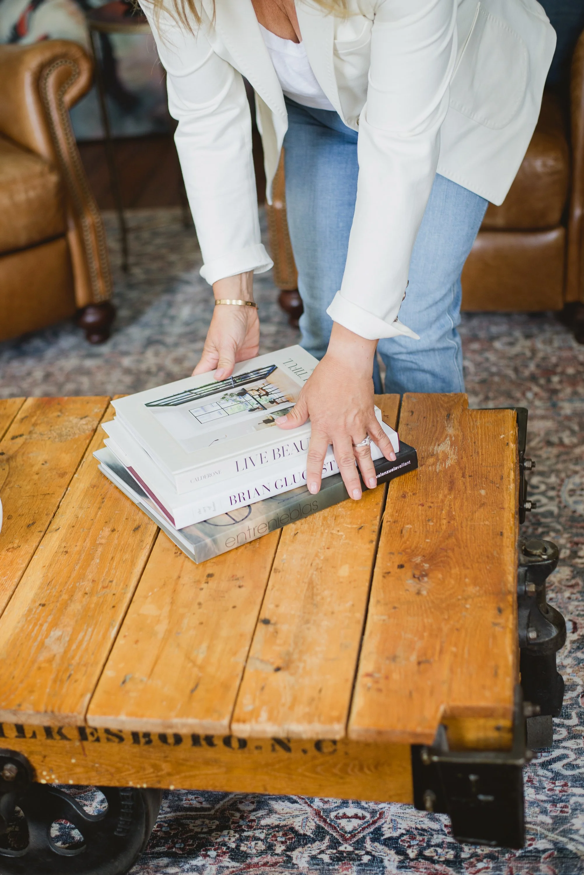 A person arranging large coffee table books on a rustic wooden table.