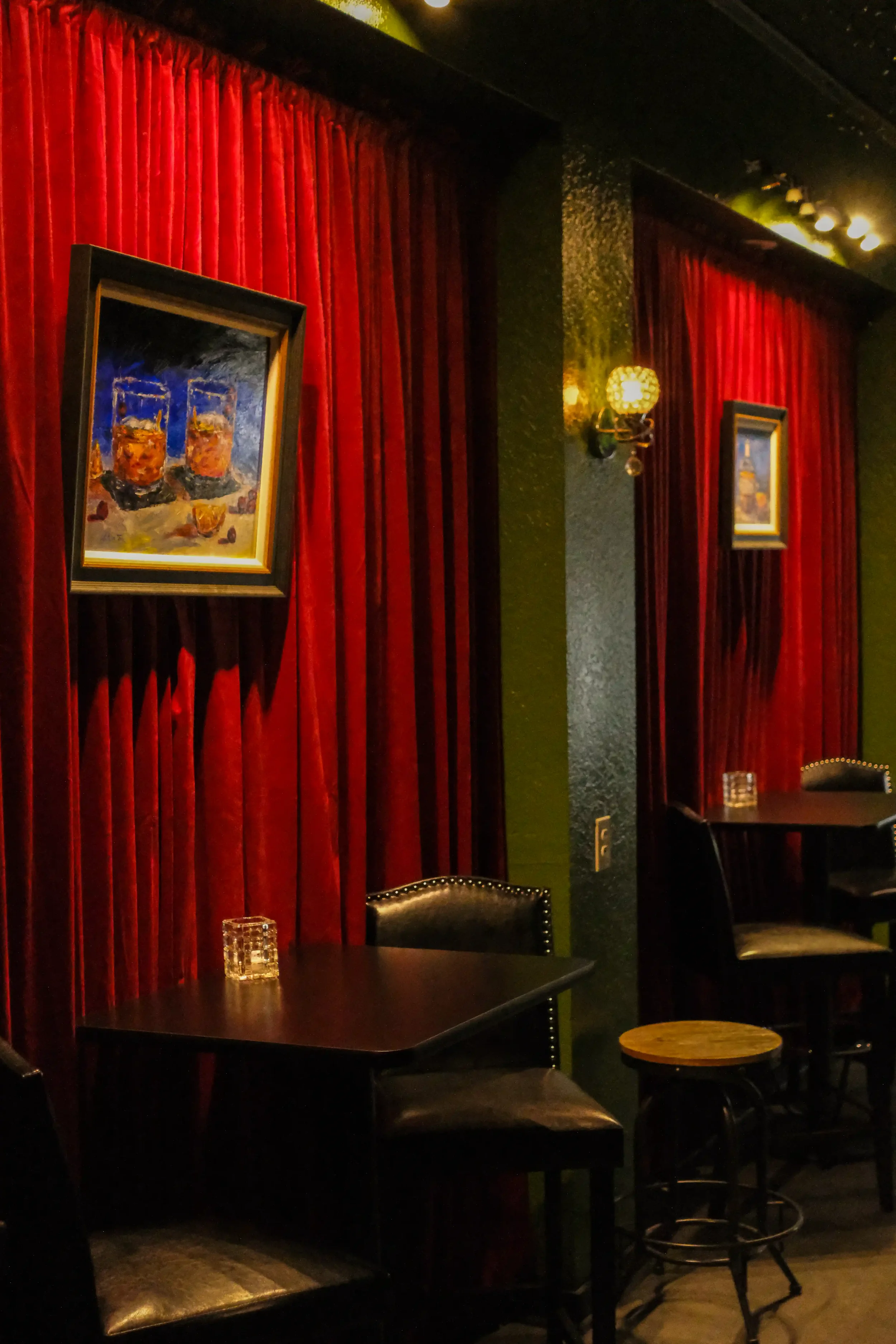 Red velvet curtains and a framed painting of cocktails hang above an intimate wooden table inside the dimly lit Lounge at The Artisan Downtown.