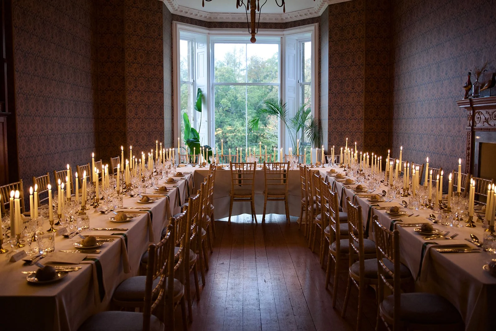 Elegant dining room with a long table set with glassware, silverware, and candles, with a large pipe organ against a patterned wall in the background.