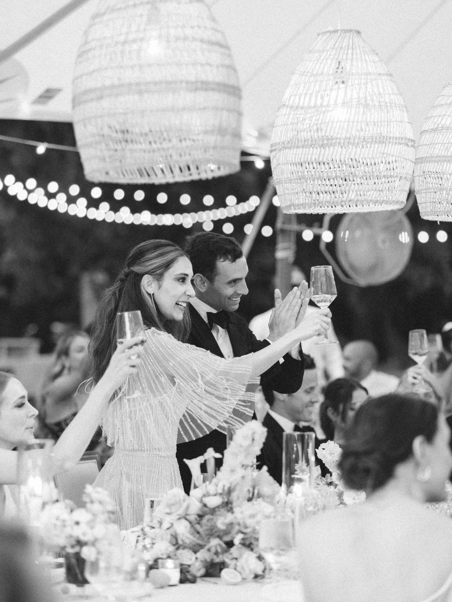 Bride and groom raise their champagne glasses in a heartfelt toast under the candlelit tented reception
