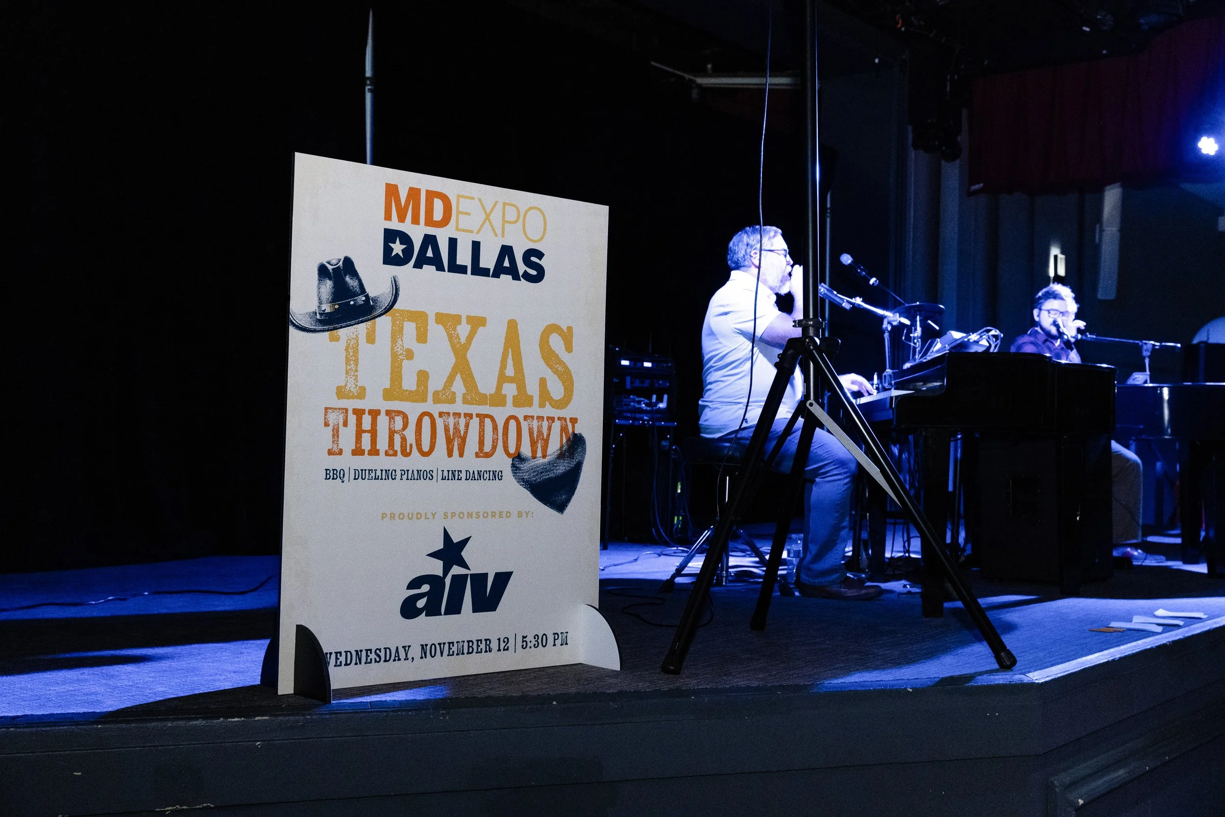 A stage with two musicians playing a keyboard and a piano, a sign promoting the Texas Throwdown event, and stage lighting.