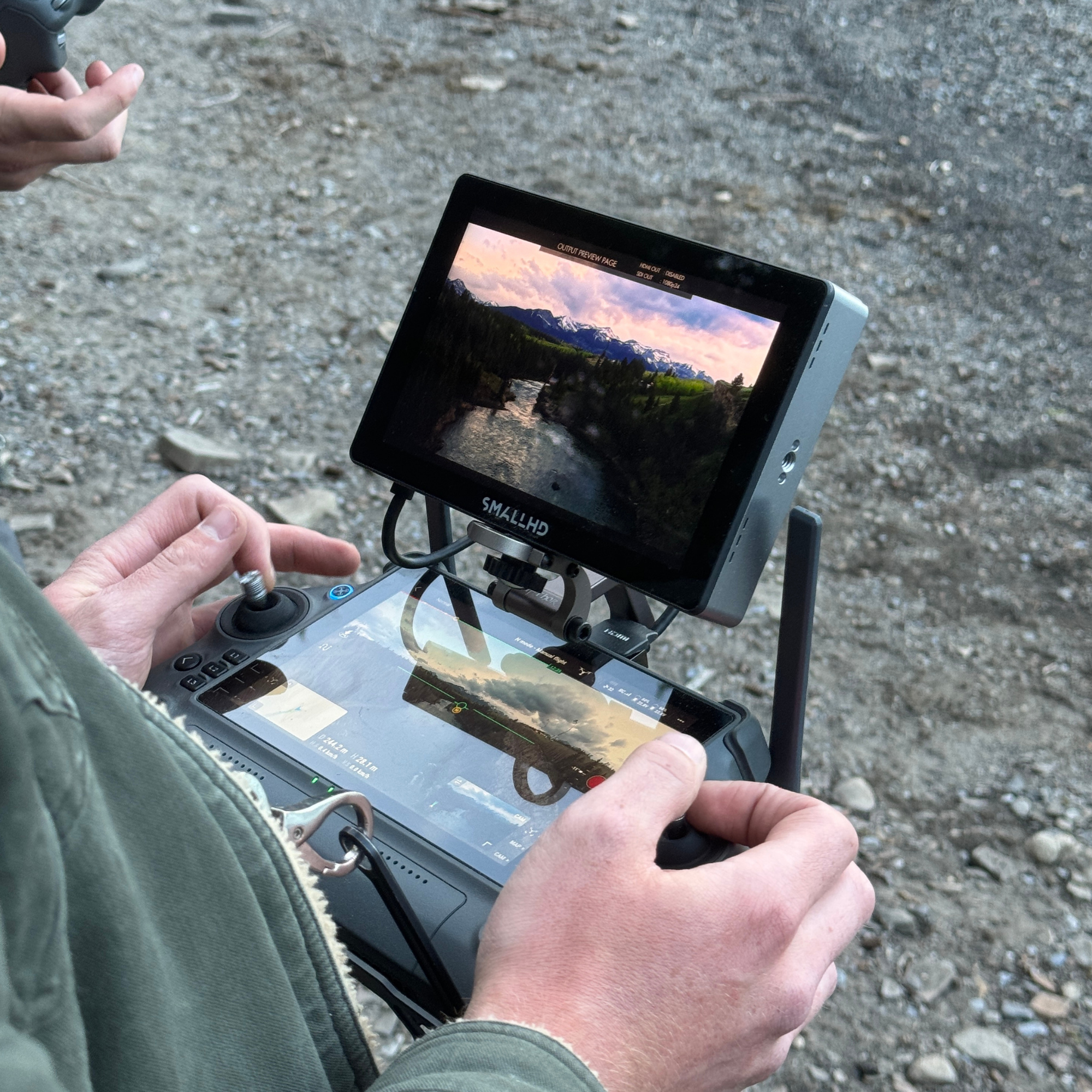 A person operating a drone with a remote control, capturing a landscape of a river surrounded by trees and mountains at sunset.