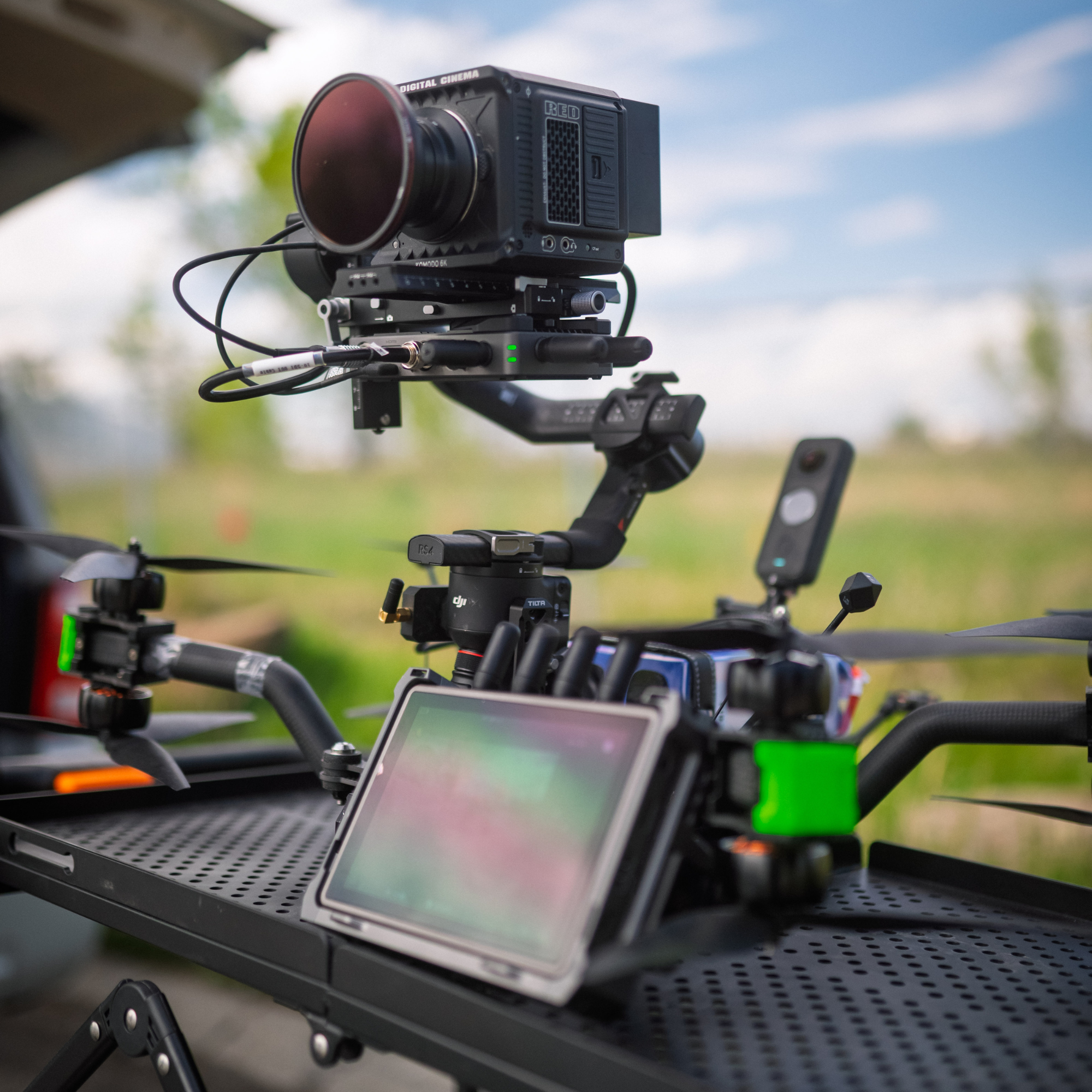 A drone equipped with a camera mounted on a stabilizer, with an external monitor and various control equipment, set outdoors with a blurred natural background.