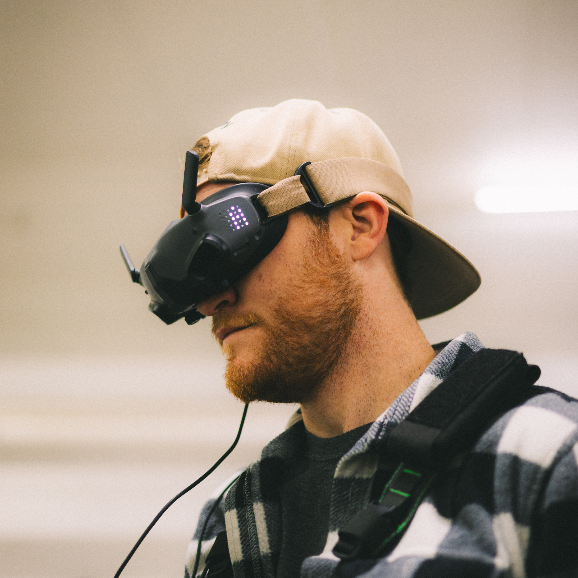 A man wearing a baseball cap, checkered shirt, and a backpack, using a virtual reality headset with headphones.