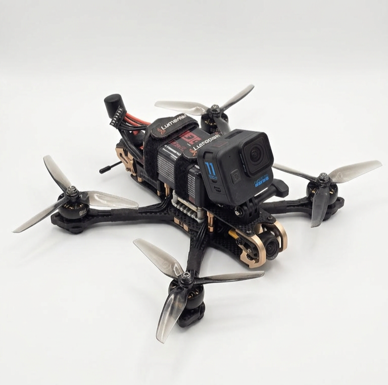 A racing drone with a mounted GoPro camera, black and bronze frame, four propellers, and electronic components visible.