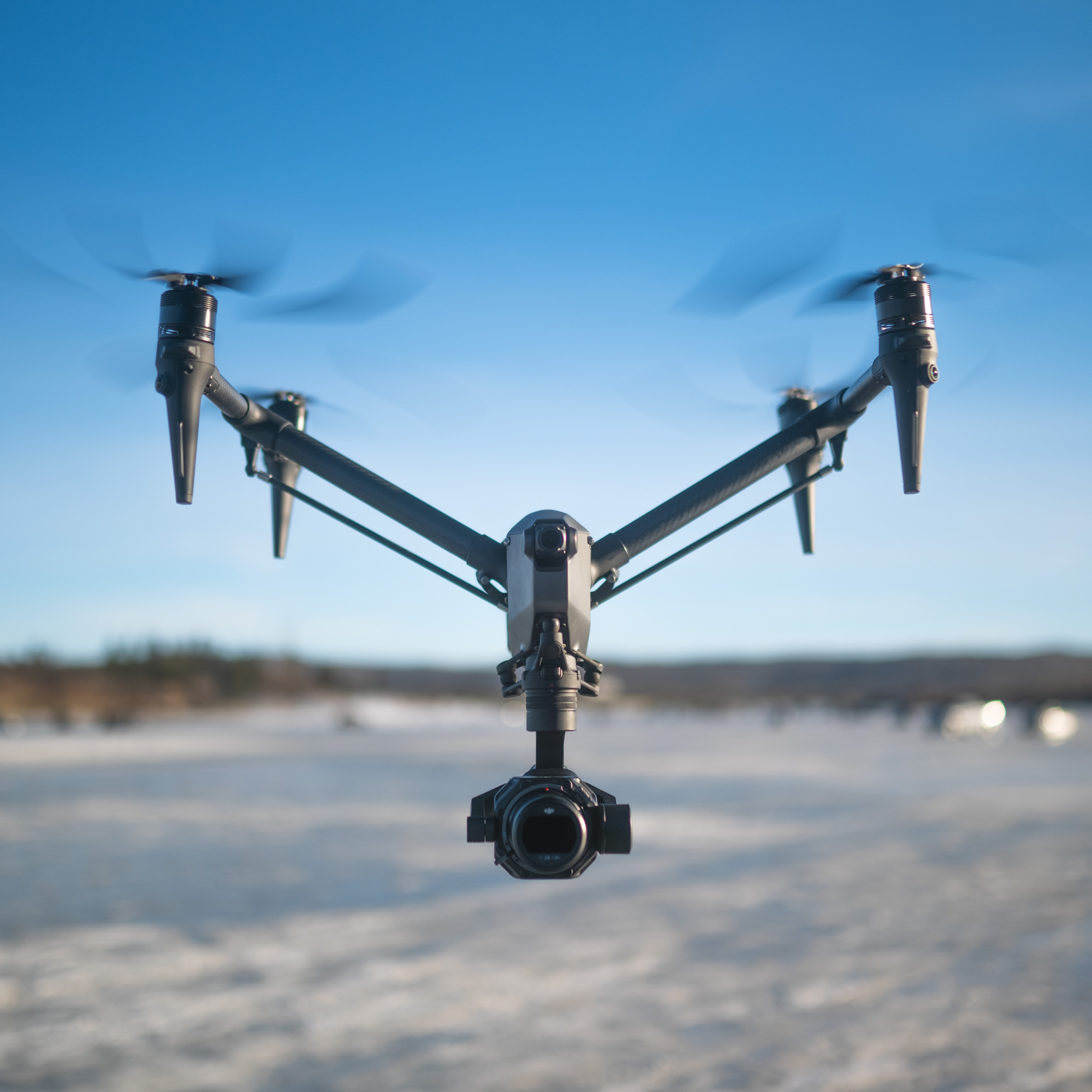 A drone with a camera attached, flying over a snowy landscape under a blue sky.