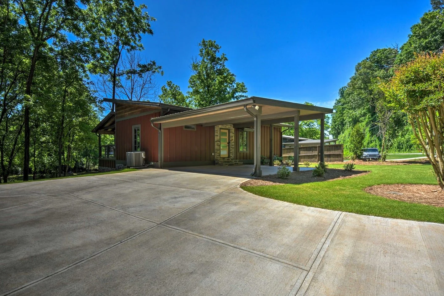 Modern house with a carport, surrounded by trees and a maintained lawn, on a sunny day.