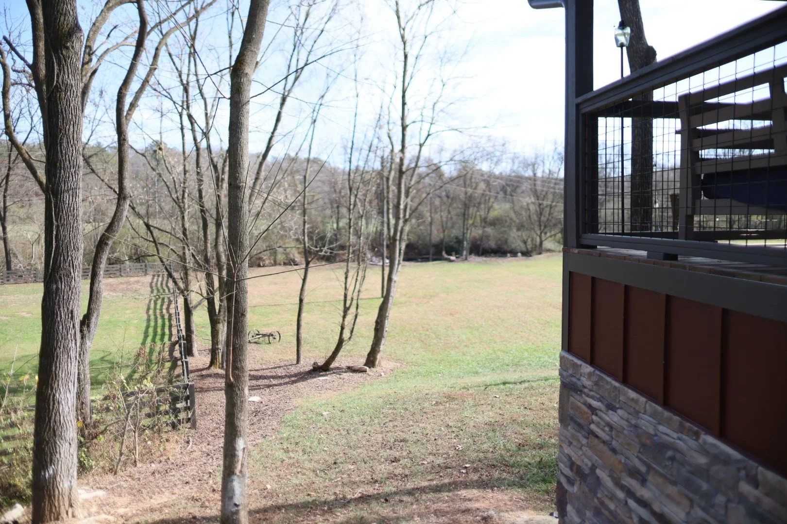 View of a grassy backyard with trees and a bicycle lying on the ground, partially seen from a patio with a railing and stone wall.