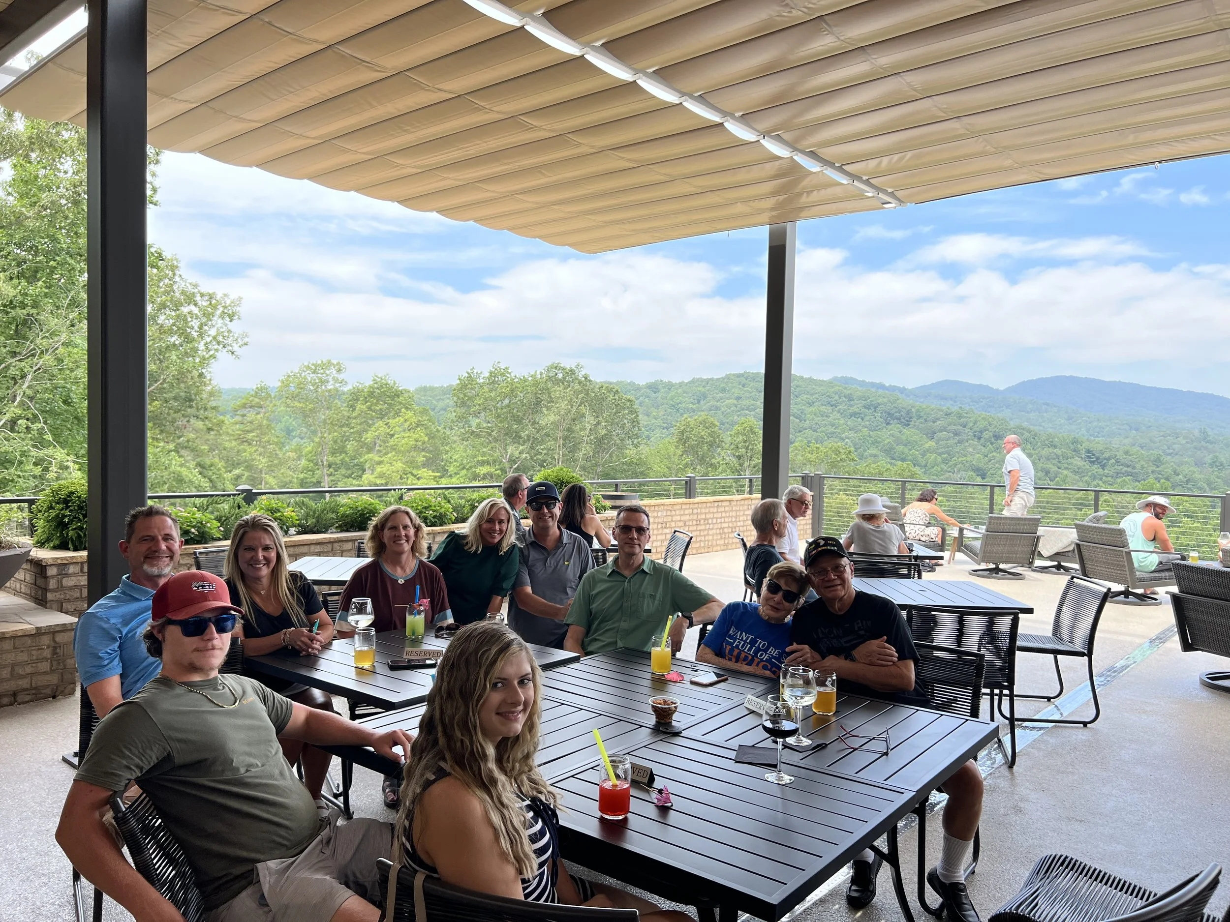 A group of people enjoying drinks and conversation at an outdoor patio with a scenic mountain view.