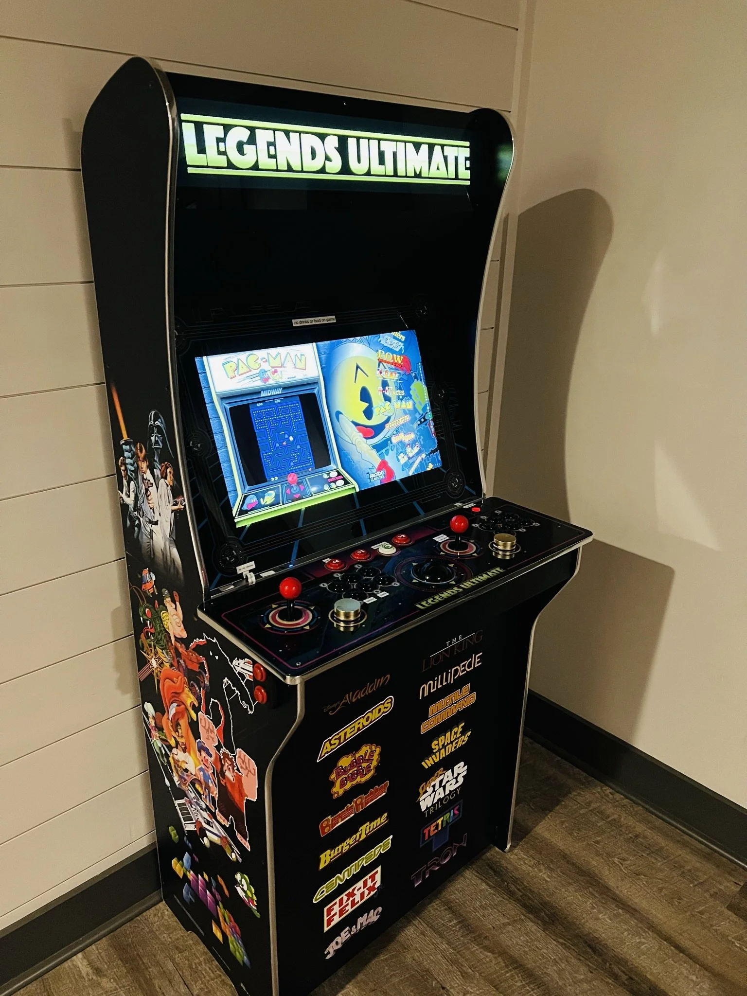 Arcade machine labeled 'Legends Ultimate' with classic video game graphics and stickers on the sides, featuring characters from Pac-Man and other arcade games.