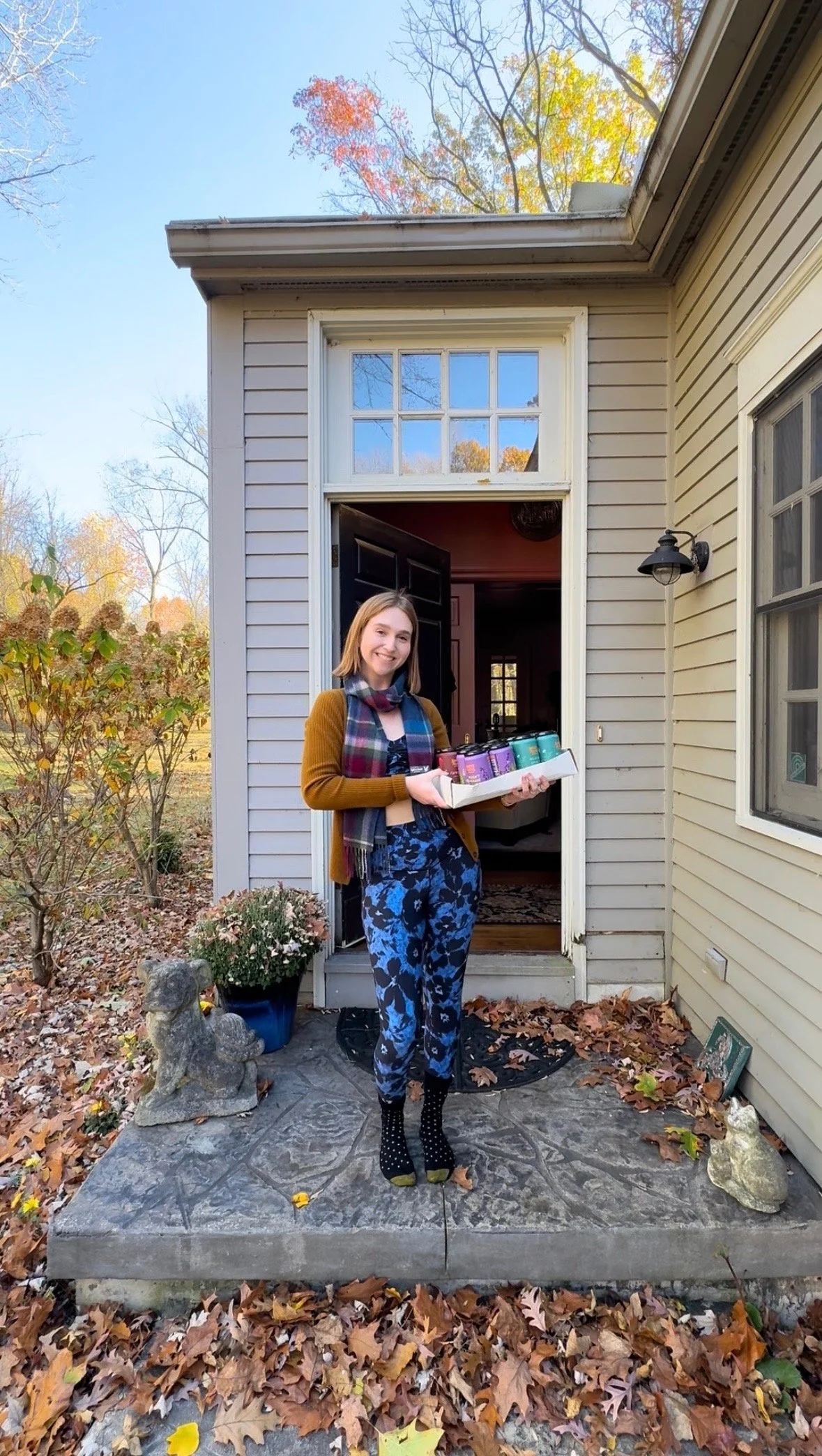 Woman stands at front door accepting her delivery of a monthly subscription from Boochy Mama's Kombucha.