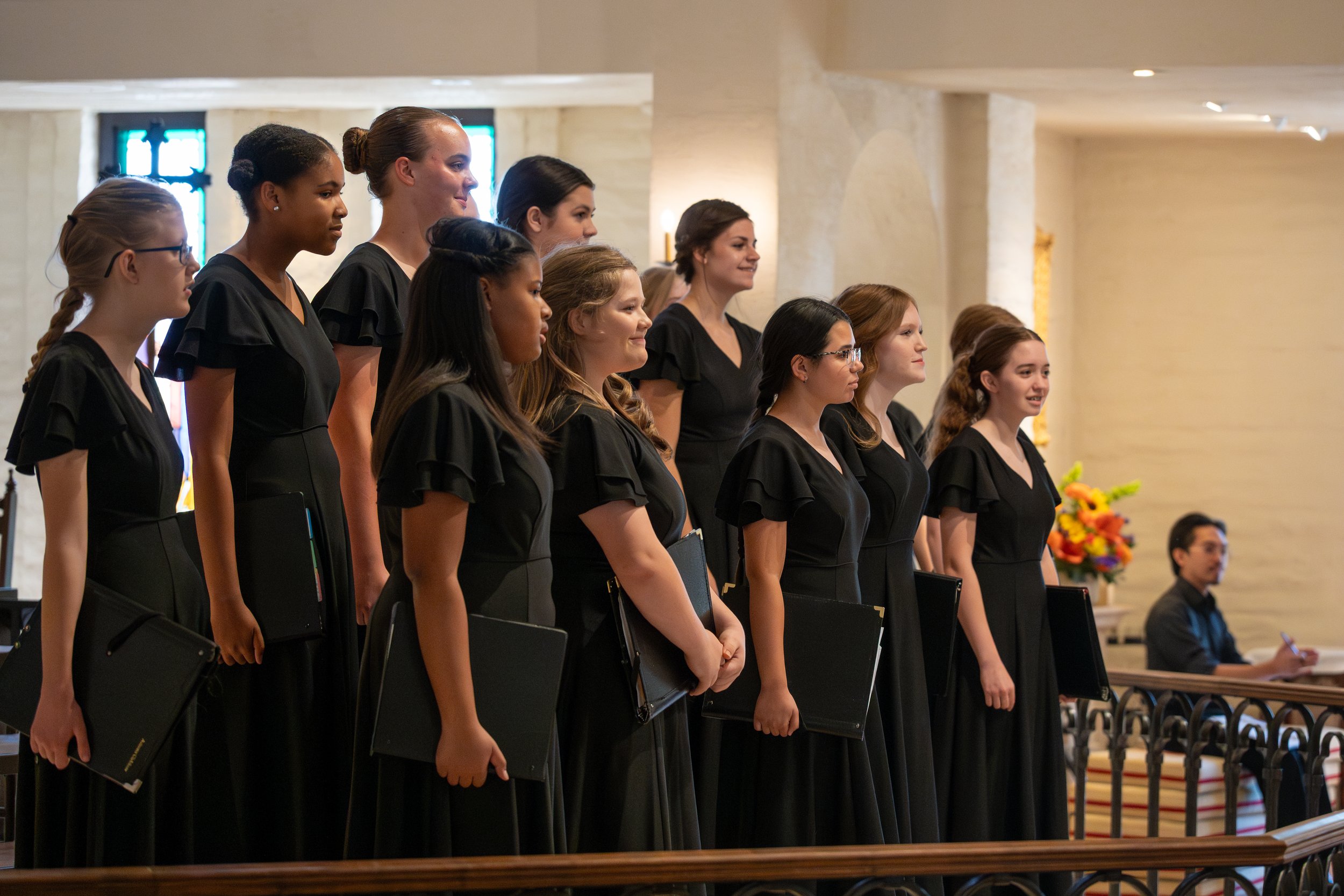 A group of women dressed in black uniforms standing in a line inside a church, holding black folders, participating in a ceremony.