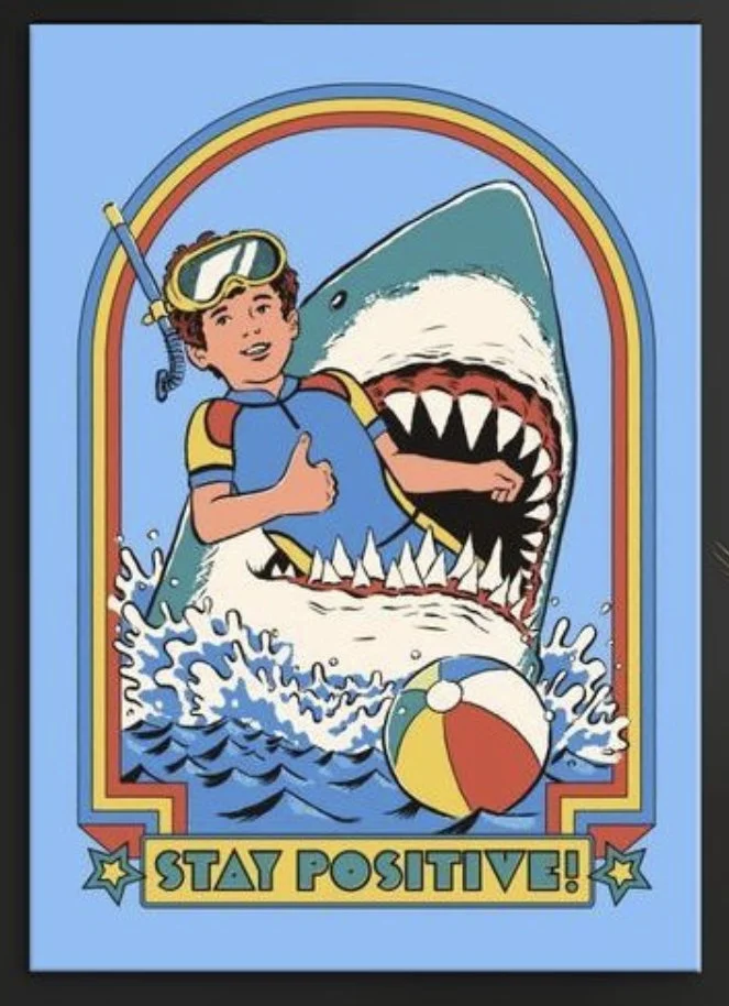 A cheerful boy wearing a snorkeling mask and life vest giving a thumbs-up, sitting inside a large, cartoonish shark's open mouth with sharp teeth, while water splashes around. There is a colorful beach ball in the water, and a rainbow in the background. The text at the bottom says, 'Stay Positive!'