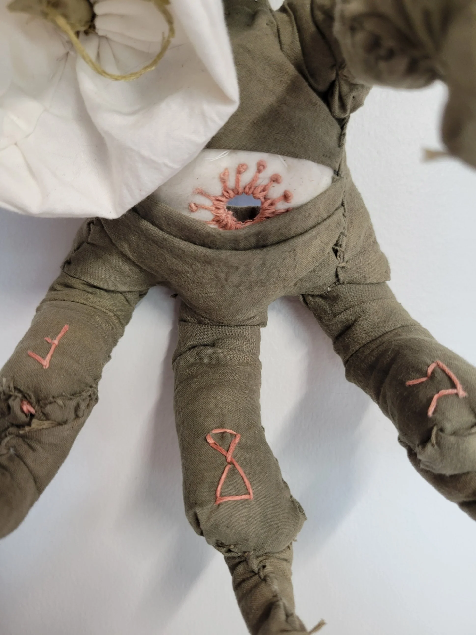 A handmade bird talon claw with embroidered symbols and a shisha mirror embroidered on its stomach, sewn with earth-toned skin, against a plain white background.