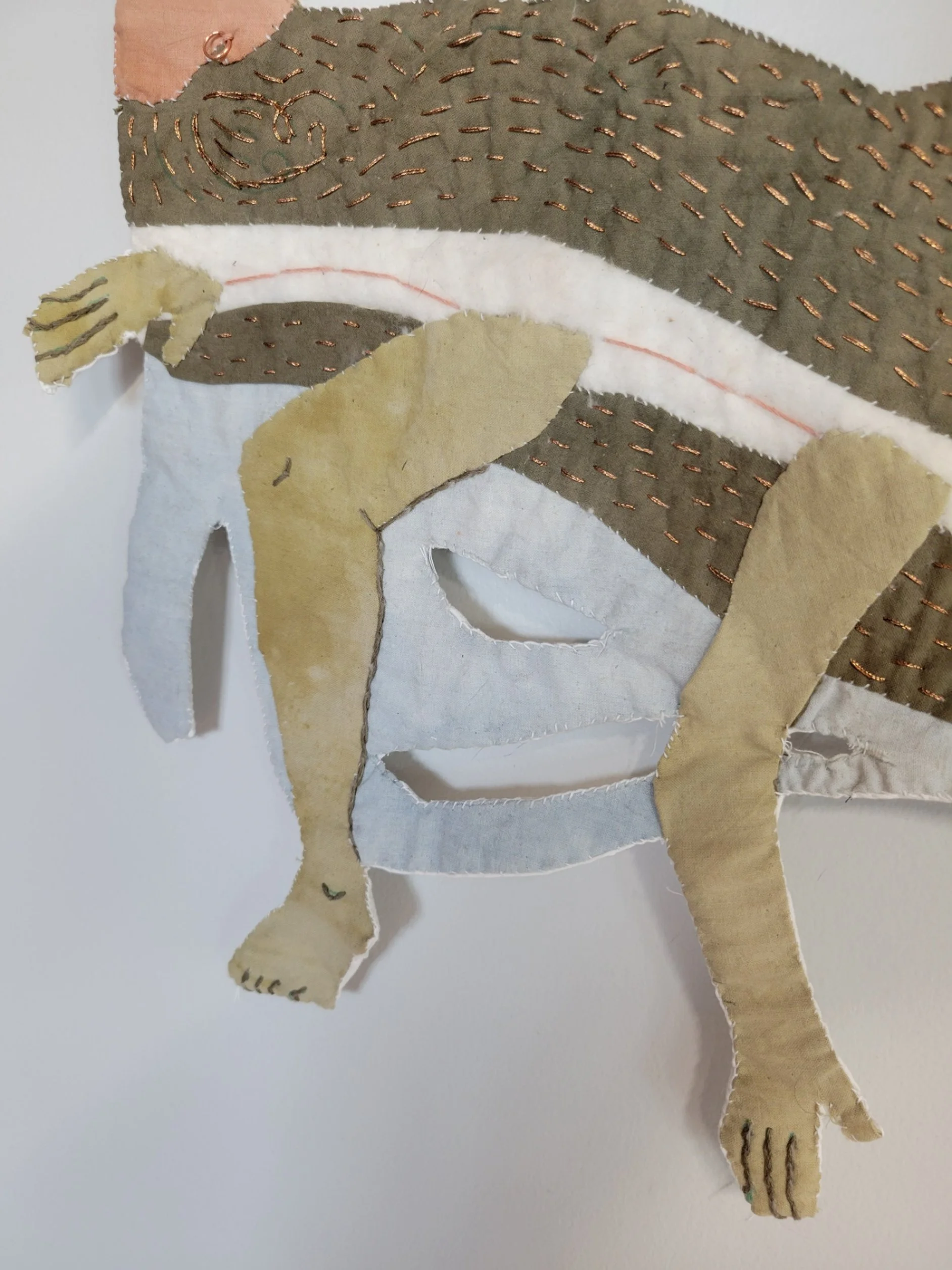 Close-up of a fabric collage art piece depicting a stylized cat face with stitched details and layered fabric pieces.