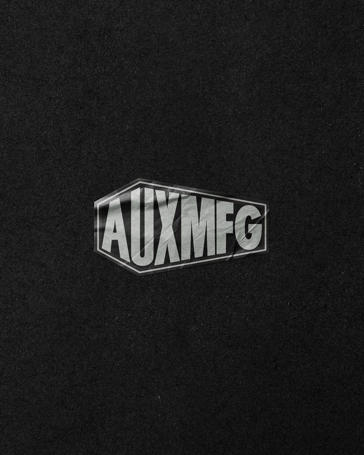 Close-up of a black fabric with a small silver and black label that reads 'AUXMEG' in bold, uppercase letters.