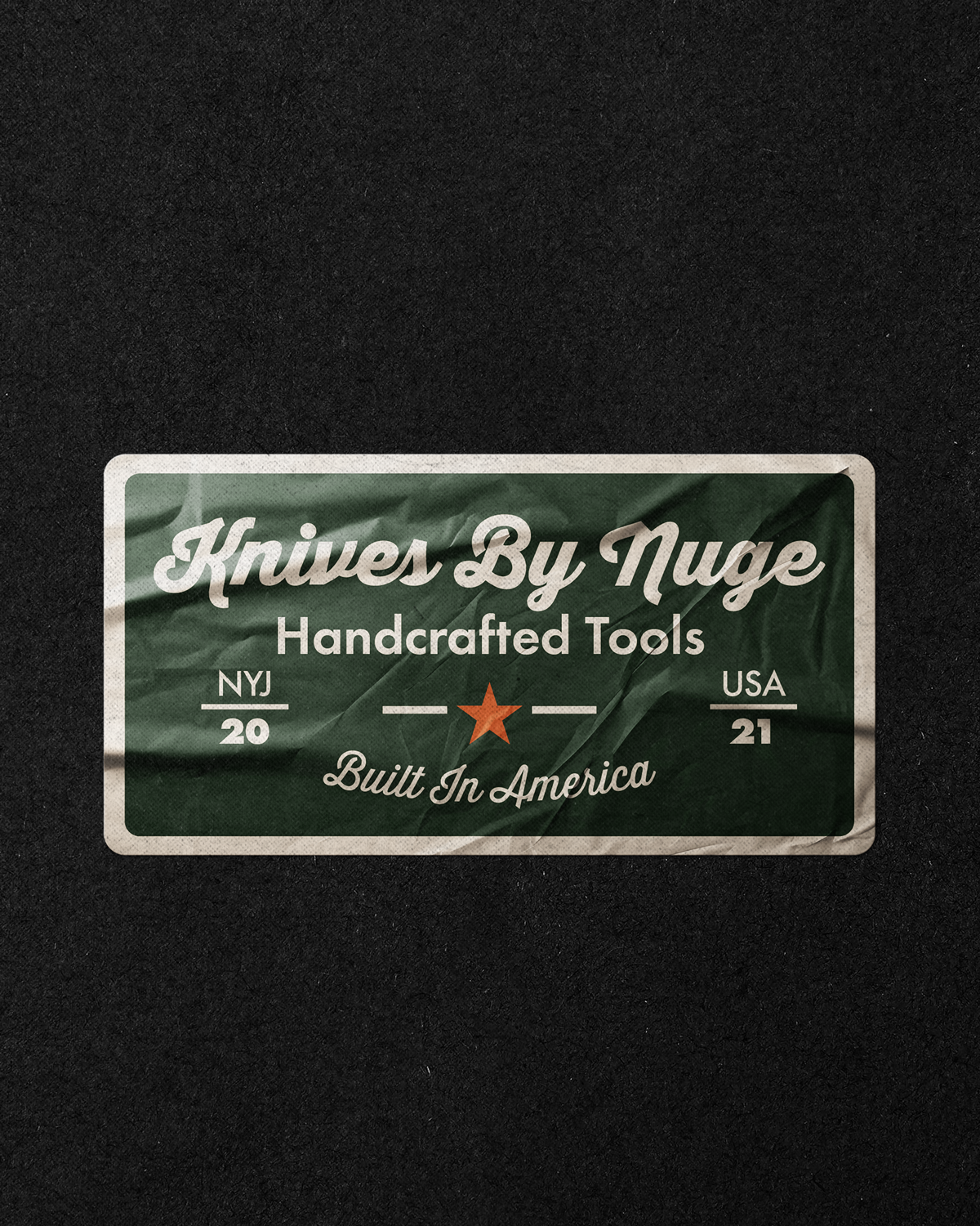 A wrinkled green paper label with white text reads 'Knives By Nuge, Handcrafted Tools, Built In America,' with a red star, and the year 'NY 20' and 'USA 21' on either side.