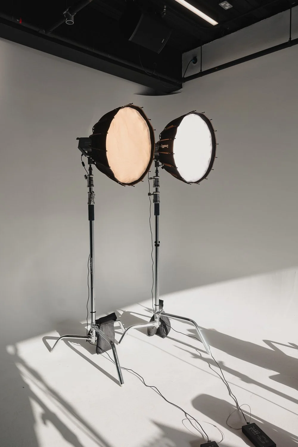 Two large studio lights on stands with power cords, directed at a plain white background.