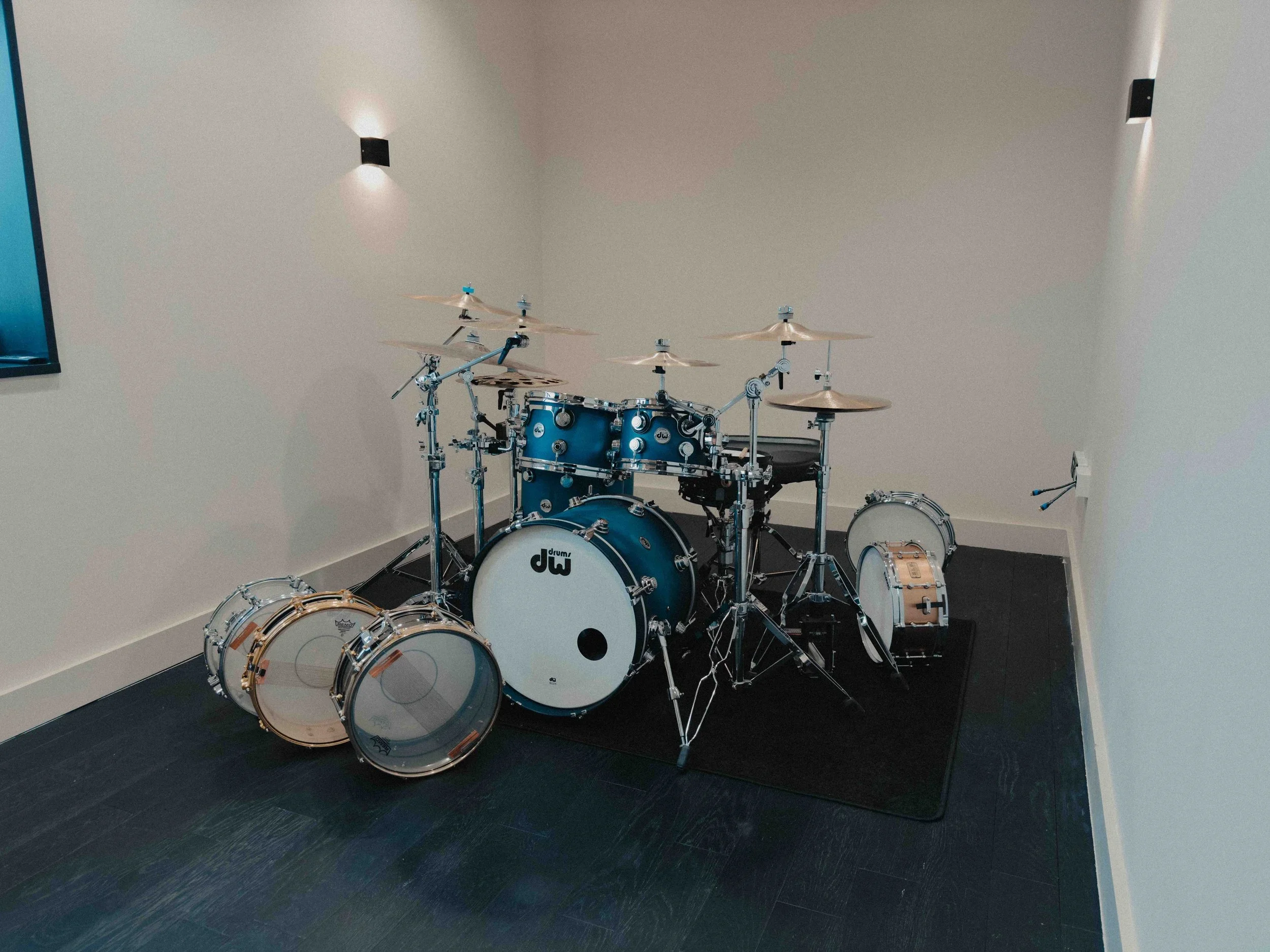 Blue drum set with cymbals, bass drums, snare, and toms on a black mat in a room with beige walls and wall-mounted lights.