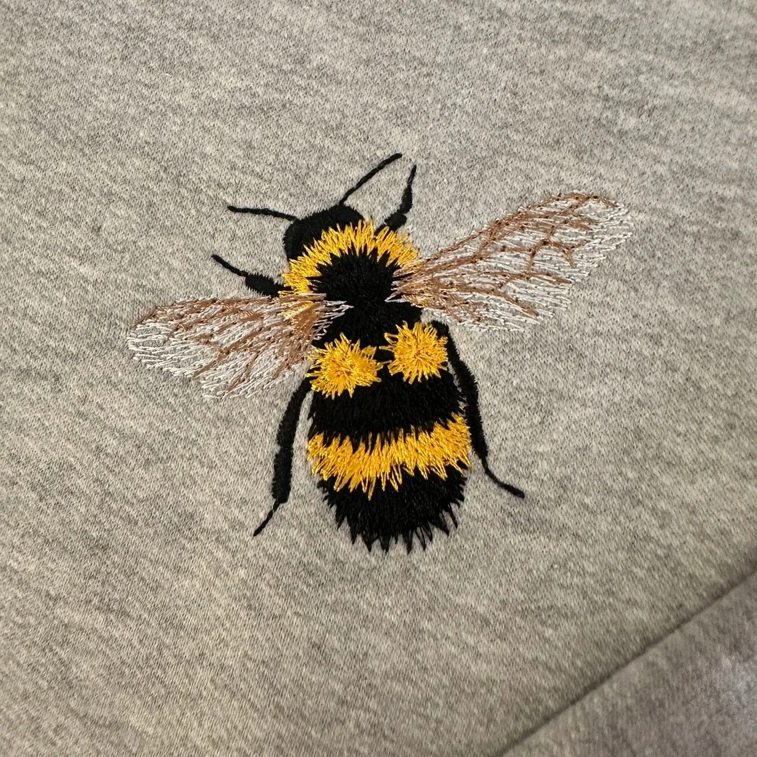 Close-up of a small embroidered bee on grey hoodie fabric.