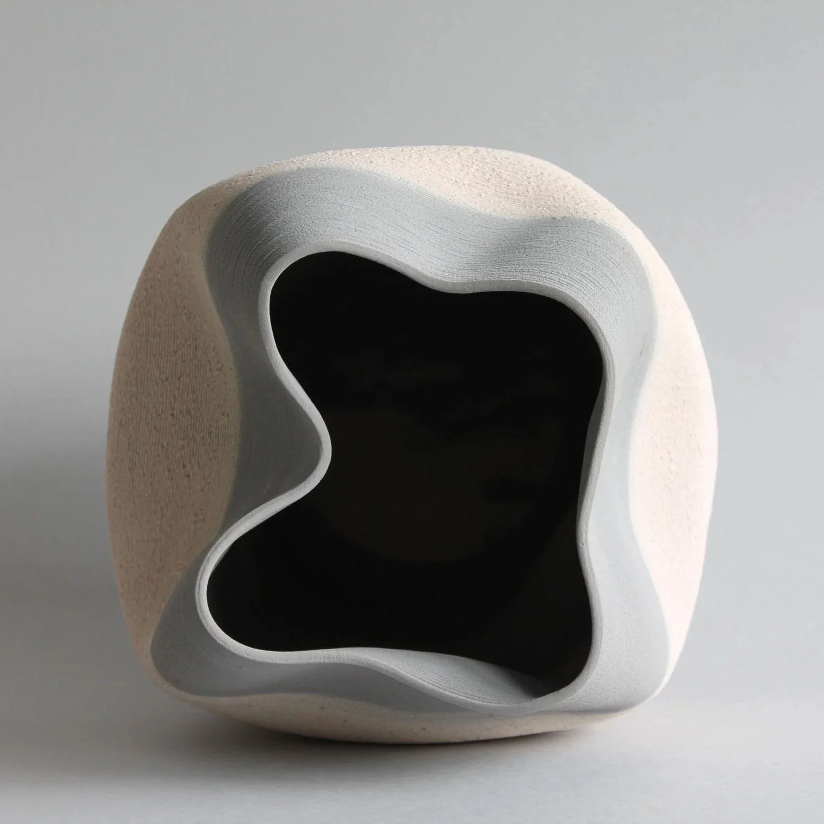 Topshot of grey and white layered design ceramic pot with large dark opening on grey background.