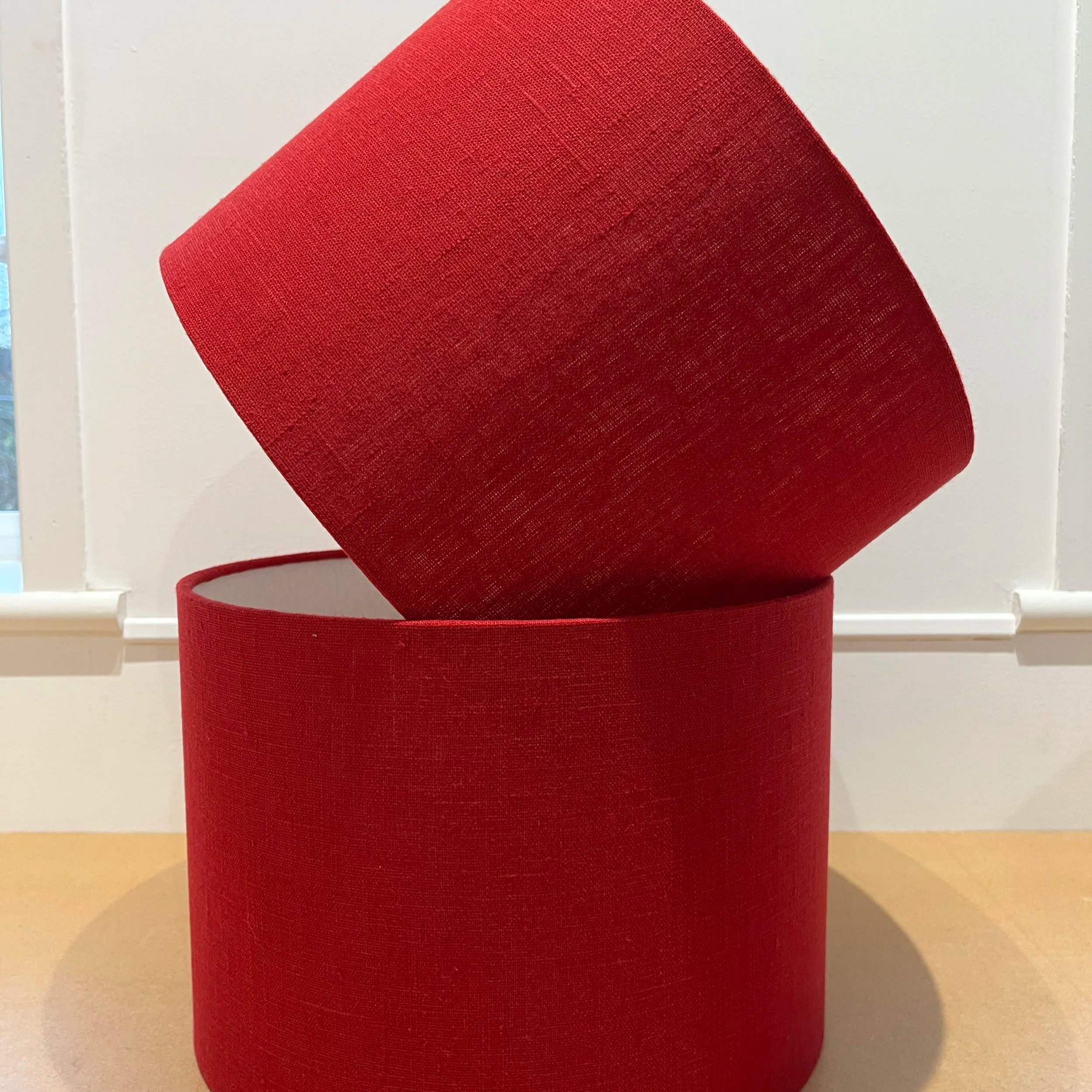Two bright red linen drum lampshades, stacked on each other