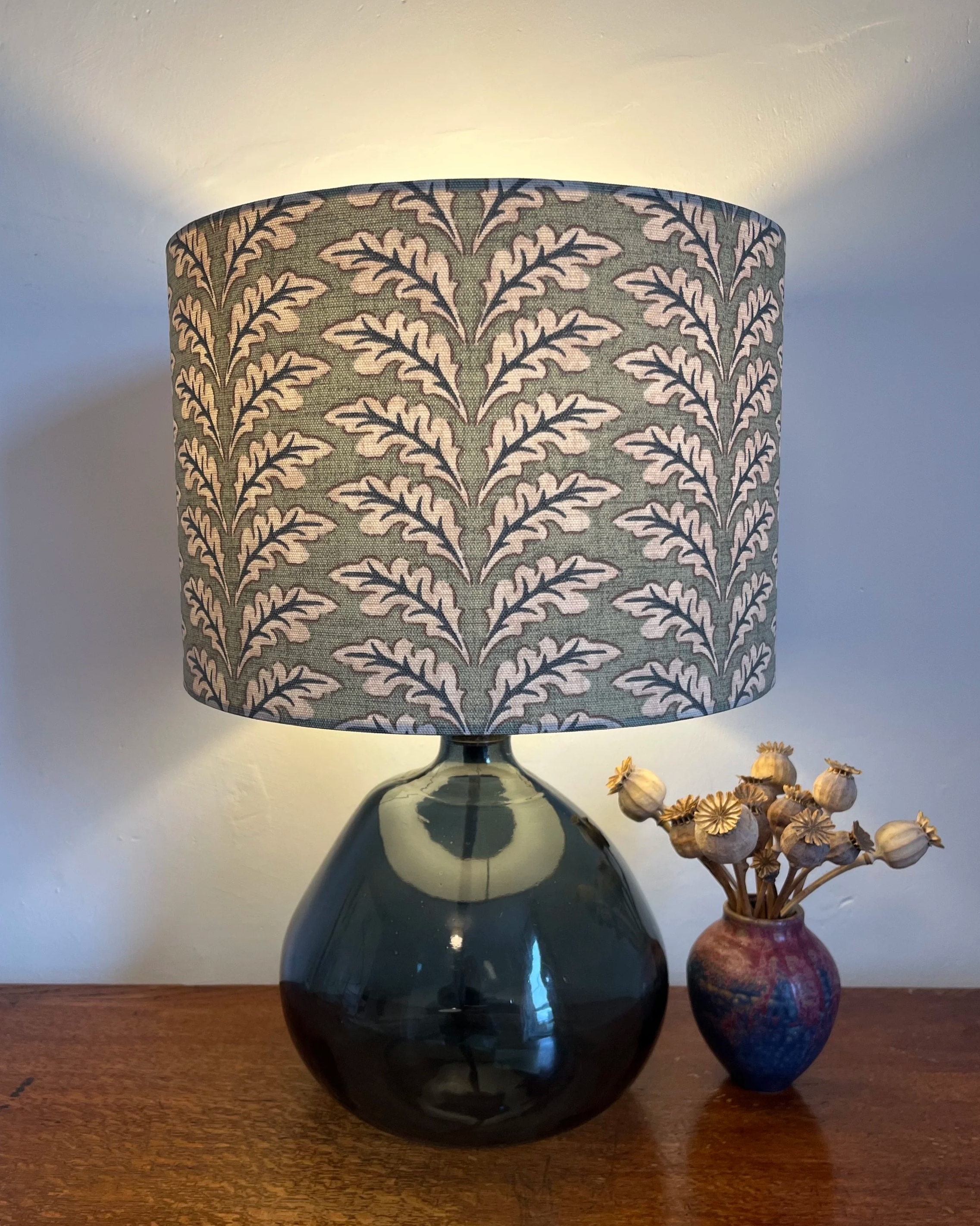 Lampshade in woodcote green leaf design, sage colour, illuminated, giving warm glow.