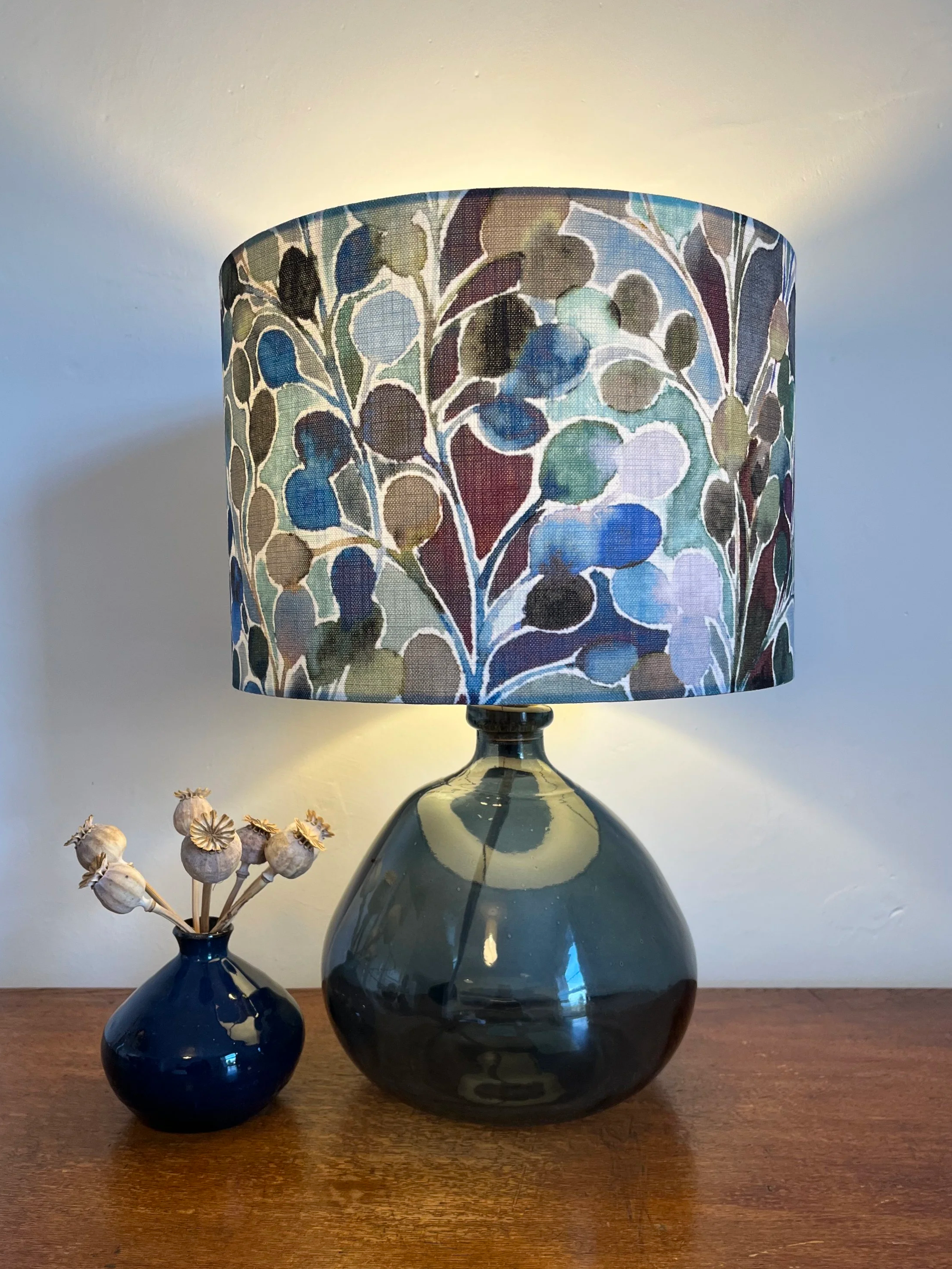 Drum table lamp shade with watercolour paint leaf design in blues, green and plum colours.