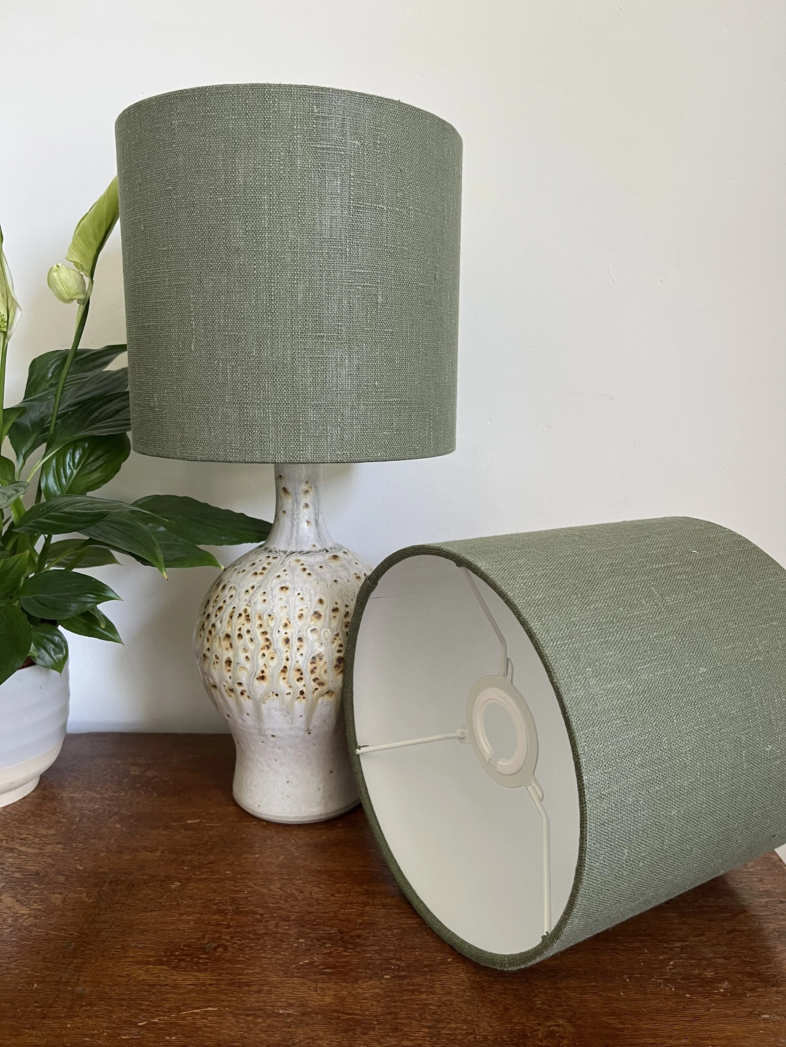Two dark green linen lamp shades, one on a lamp, the other on its side to show the EU to UK fitting.