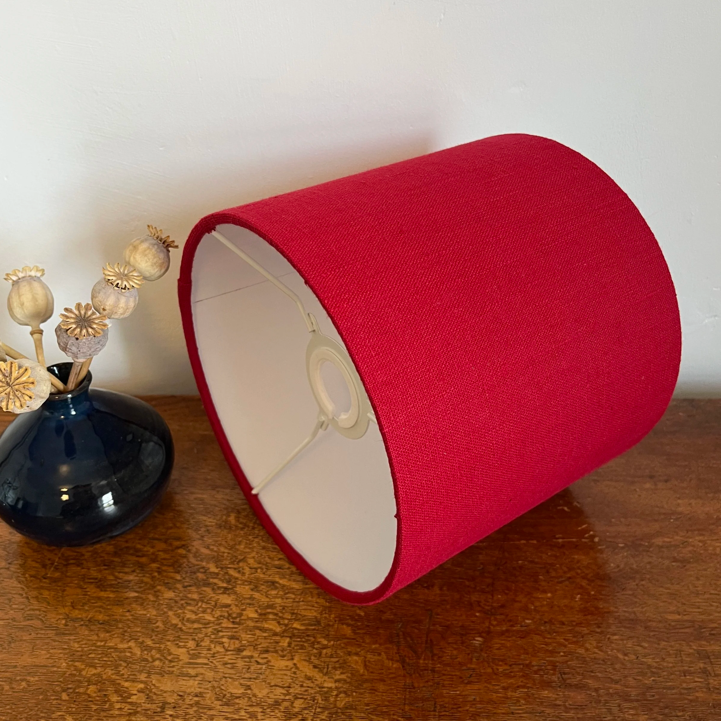 Scarlet red linen, drum lampshade on it's side, showing white lining and EU, UK lamp fitting