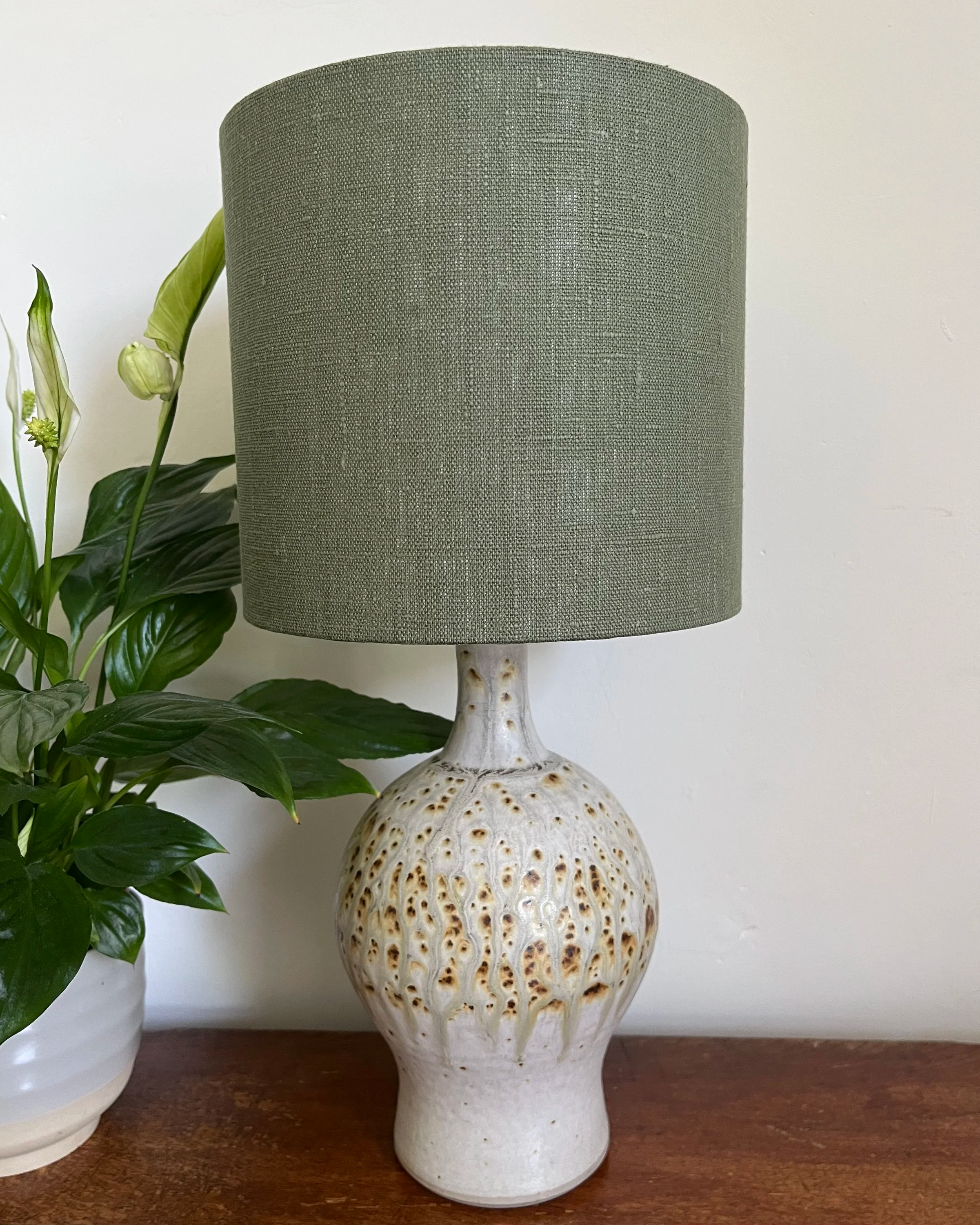 Dark green linen drum lampshade, displayed on a ceramic lamp