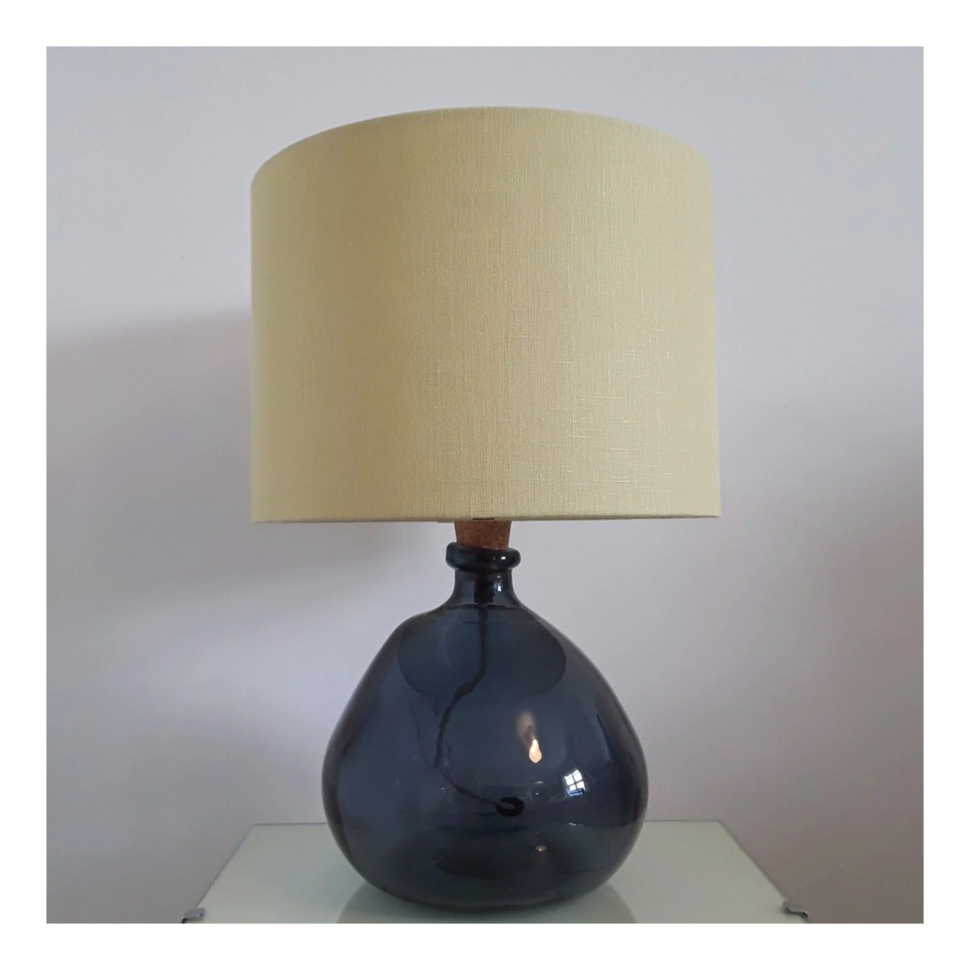 Pale yellow, linen lampshade, displayed on a dark blue glass base.