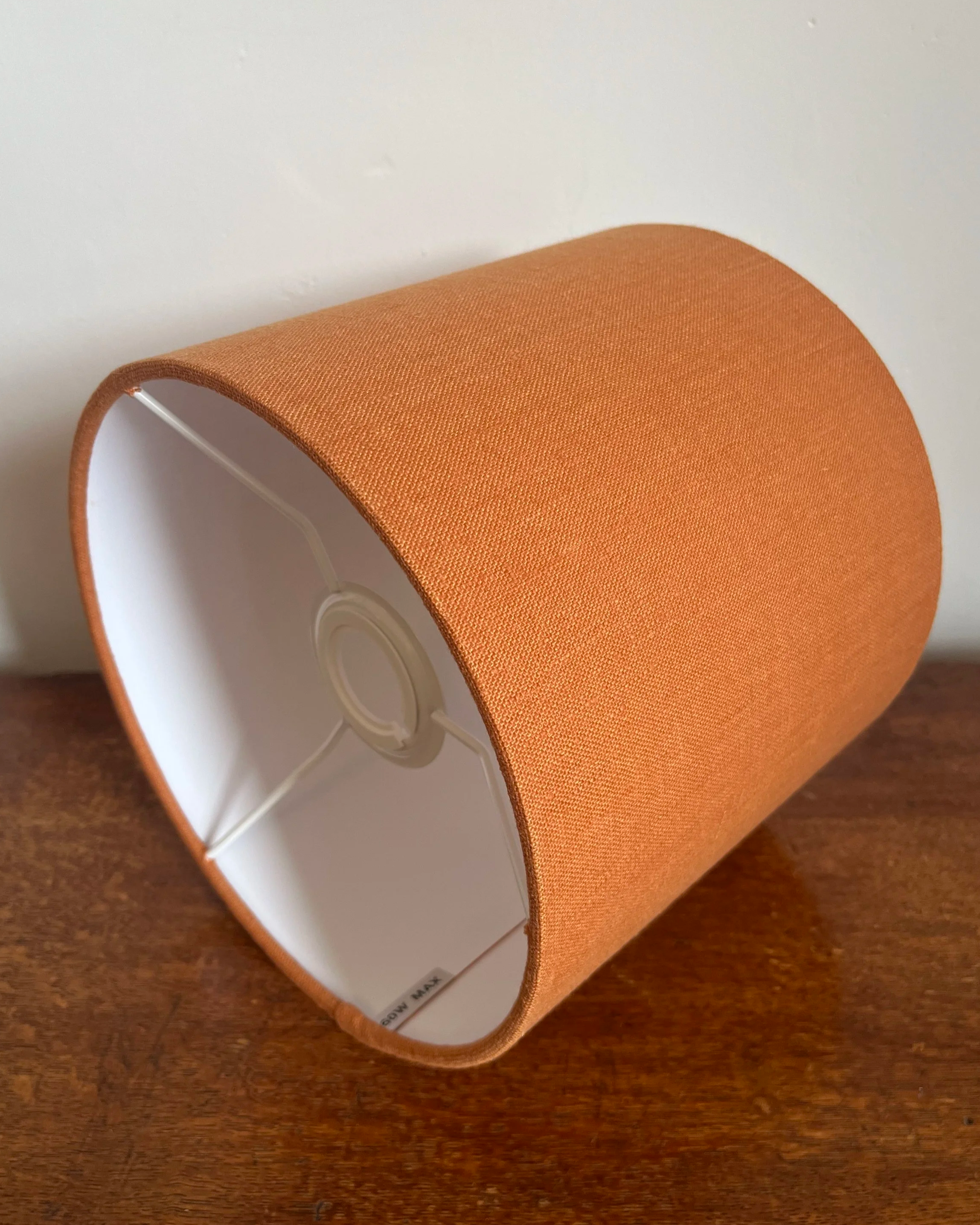 Seville orange drum lampshade, made with linen and a white lining, laying on its side to show the UK to EU lamp fitting