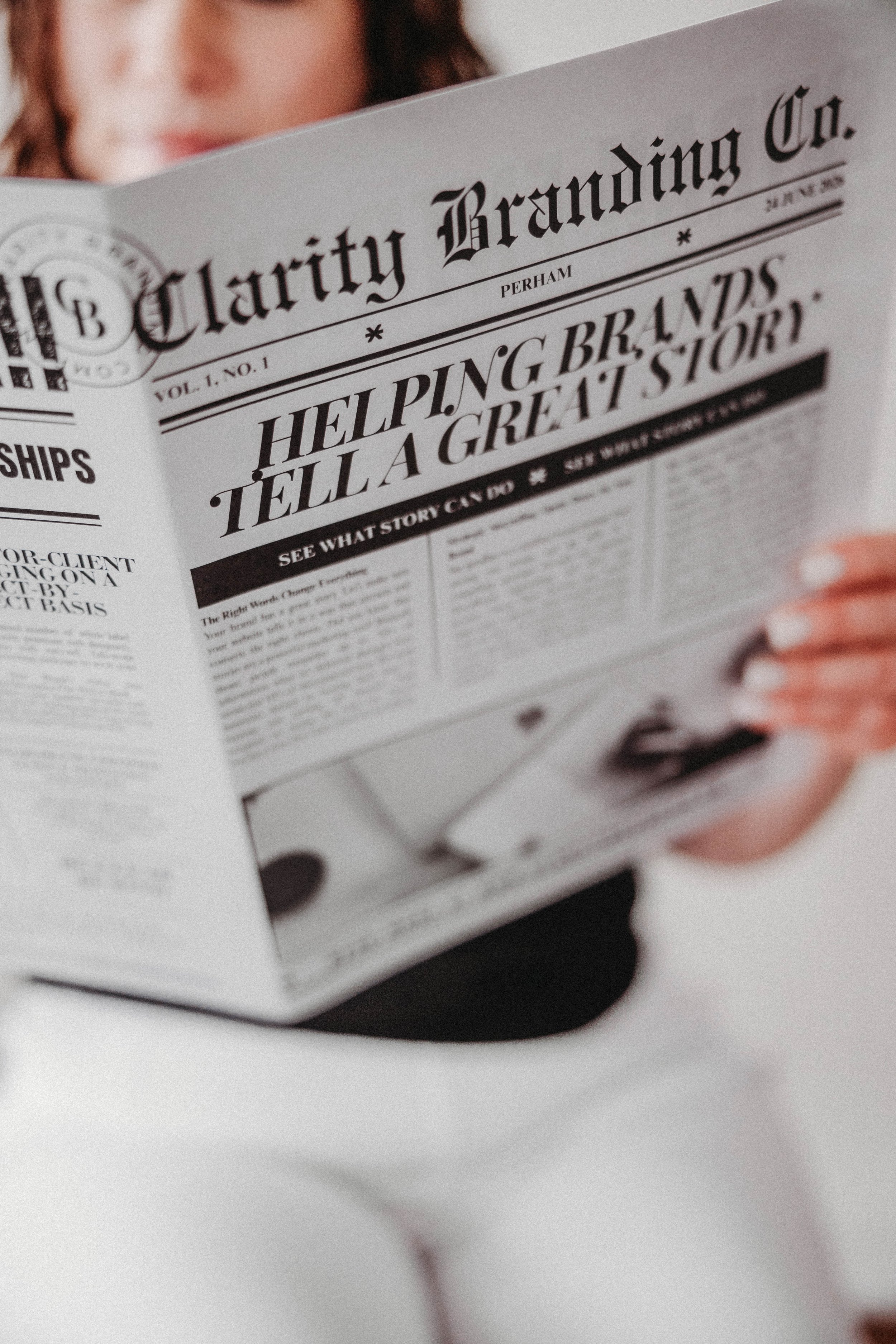 Owner Nikki Thompson reading newspaper titled 'Clarity Branding Co.' with headlines 'Helping Brands Tell a Great Story' and 'See What Story You Can'.