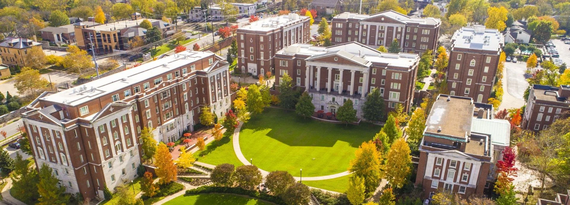 Aerial view of a college campus with red brick buildings, green lawns, and trees with fall foliage.