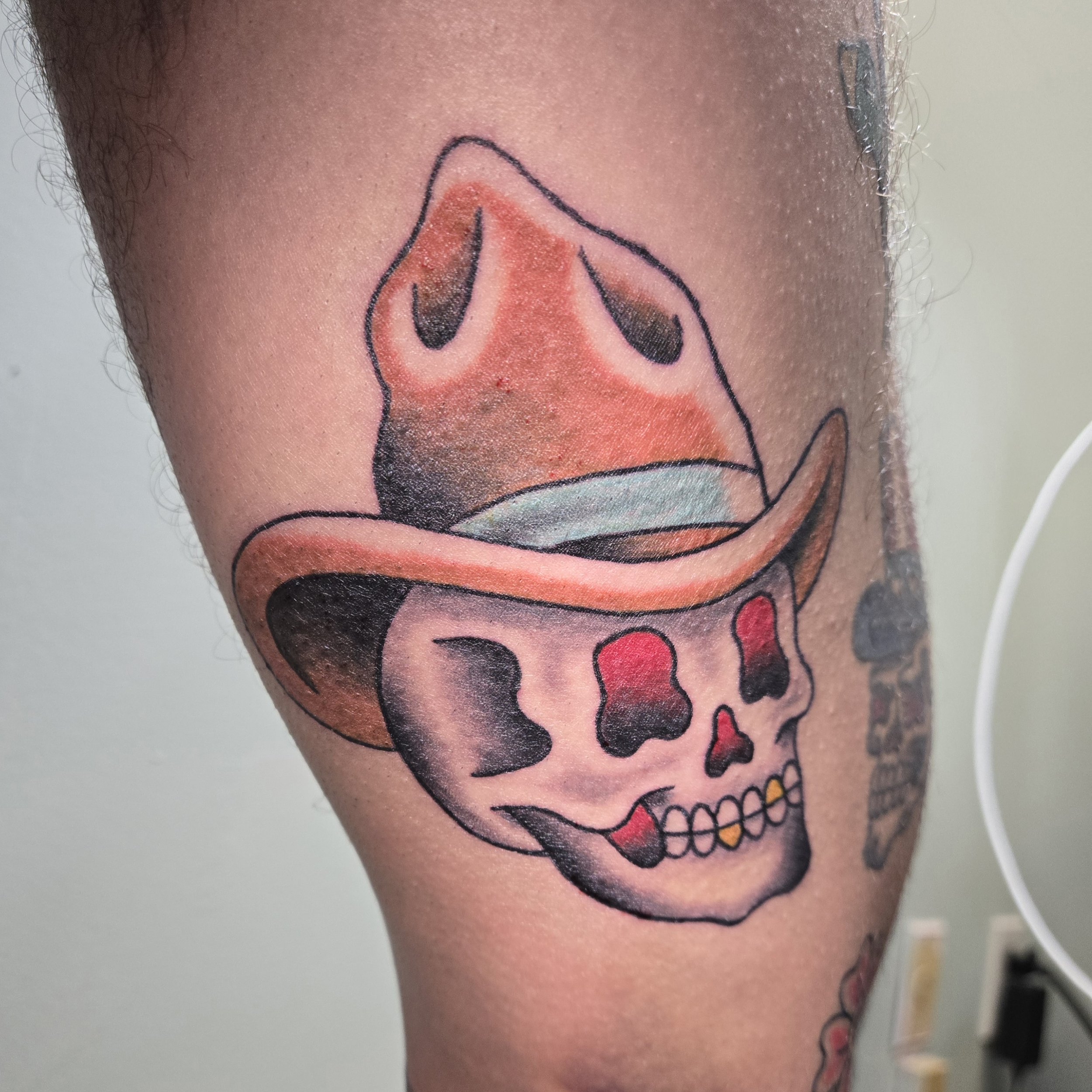 Tattoo of a smiling skull wearing a cowboy hat and a red nose, on a person's arm.