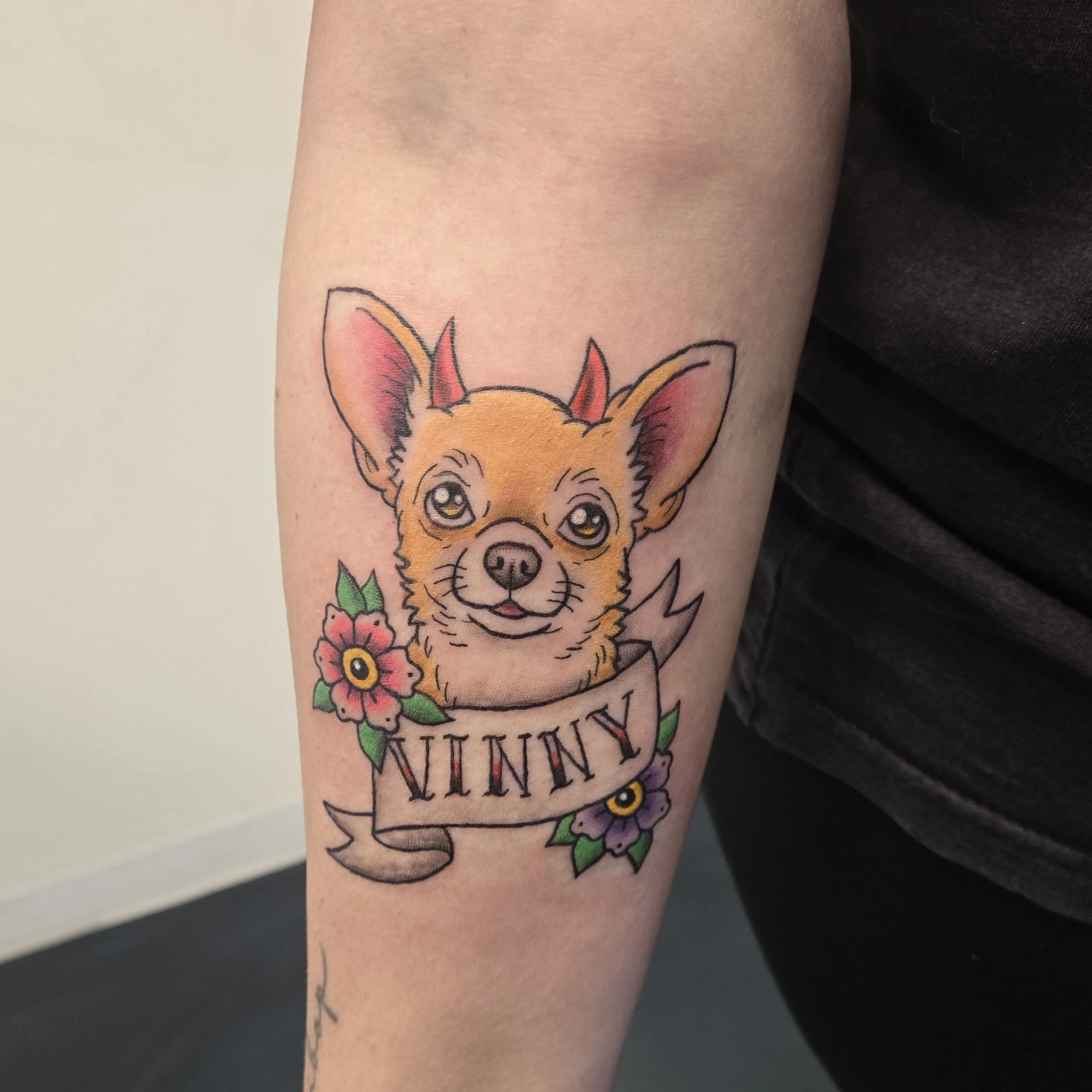 Tattoo of a chihuahua dog with large ears, surrounded by pink and purple flowers, and a banner with the name 'KUNNI'.
