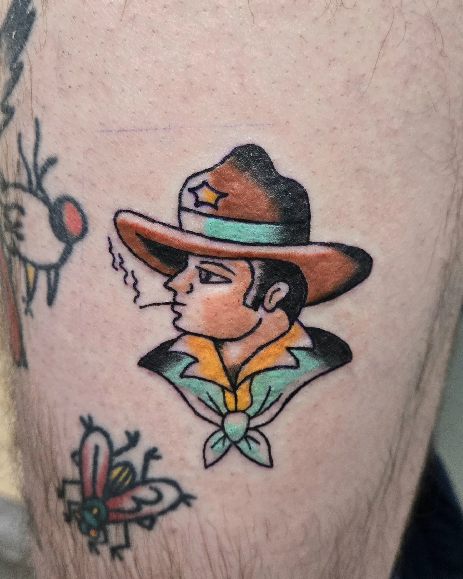 Tattoo of a person in cowboy attire with a large hat, smoking a cigarette, with a colorful neckerchief.