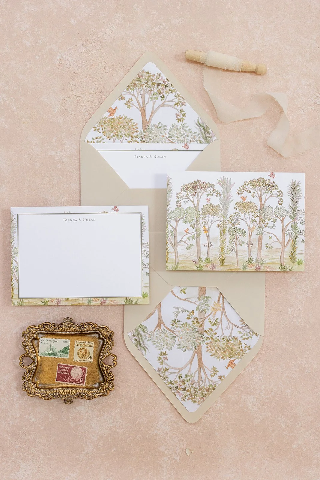 Set of stationery and vintage postage stamps on a pink background. Includes an invitation card, a matching envelope, and illustrated paper with trees and nature scenes.