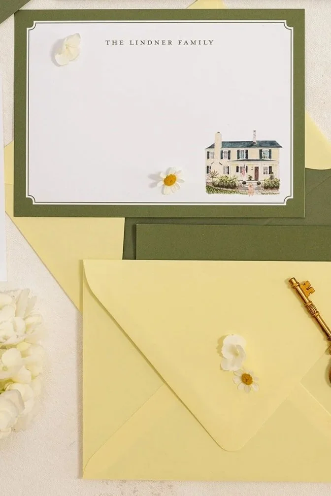 A green and yellow stationery set including a card from the Lindner family with an illustration of a house, a matching yellow envelope with a daisy and a faux daisy flower, a gold key, and white flower petals.