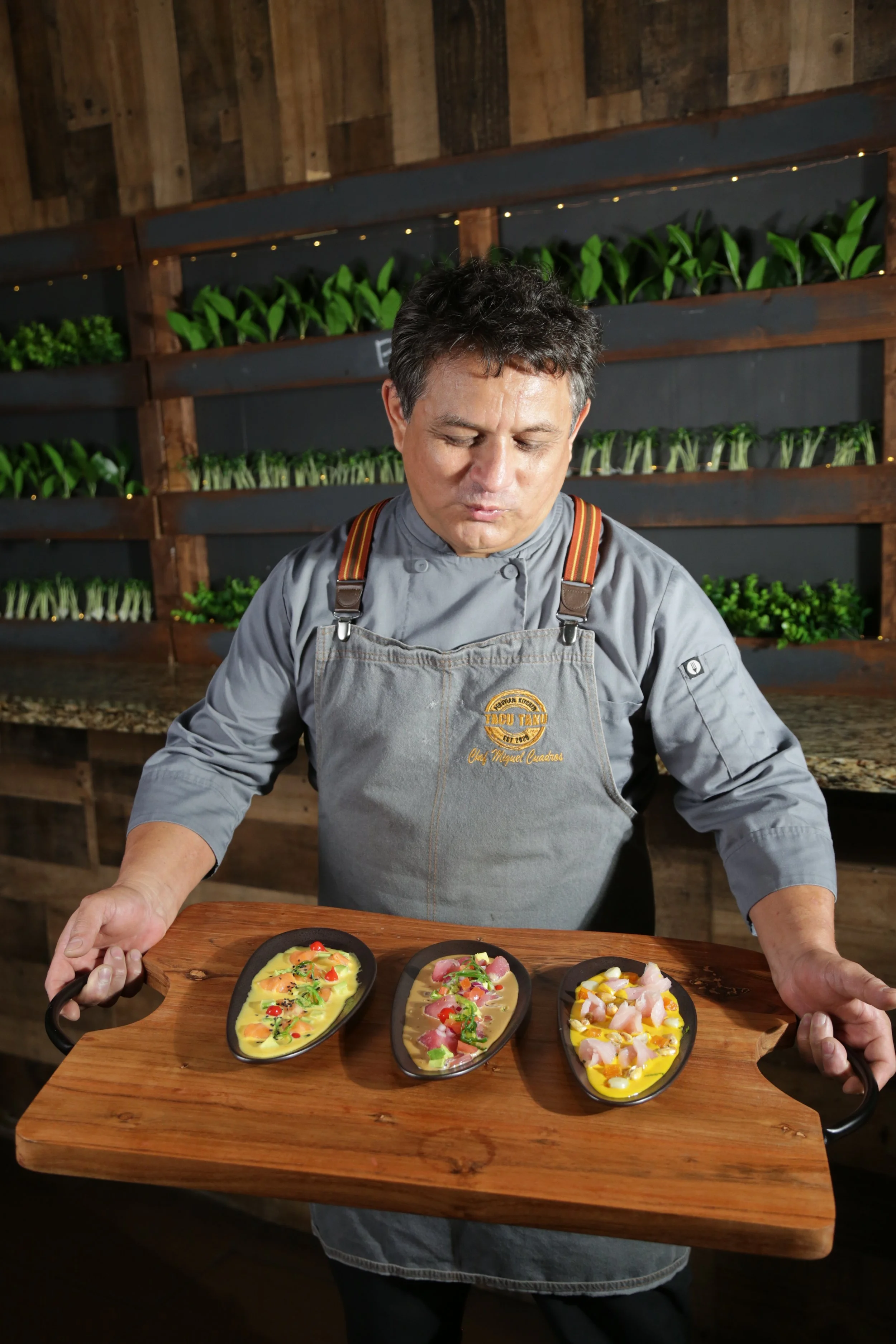 Chef Miguel Cuadros presenting three Peruvian tiraditos dishes on a wooden board