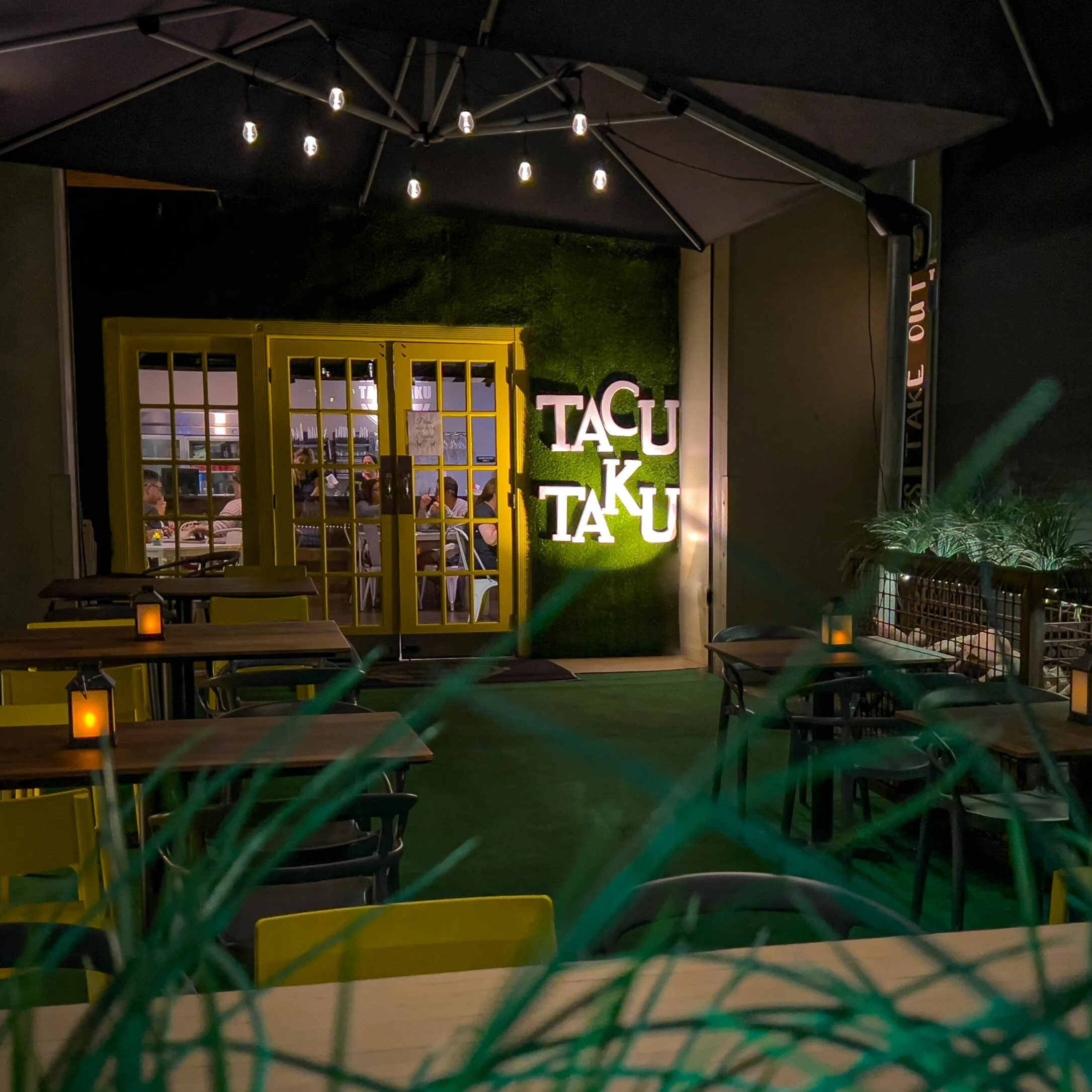 Tacu Taku patio at night with string lights, yellow doors and illuminated sign
