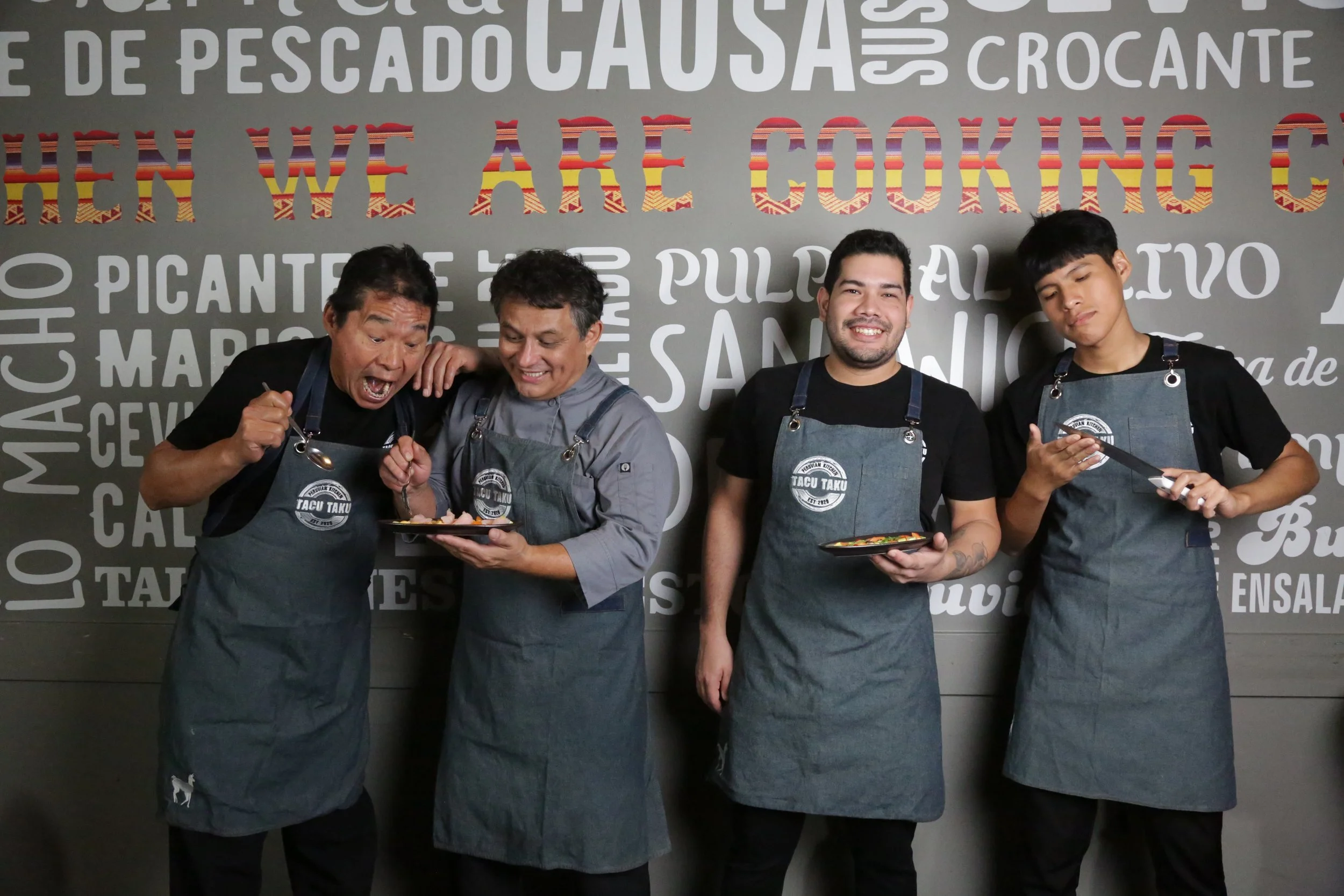 Tacu Taku kitchen crew in aprons in front of Peruvian menu mural.
