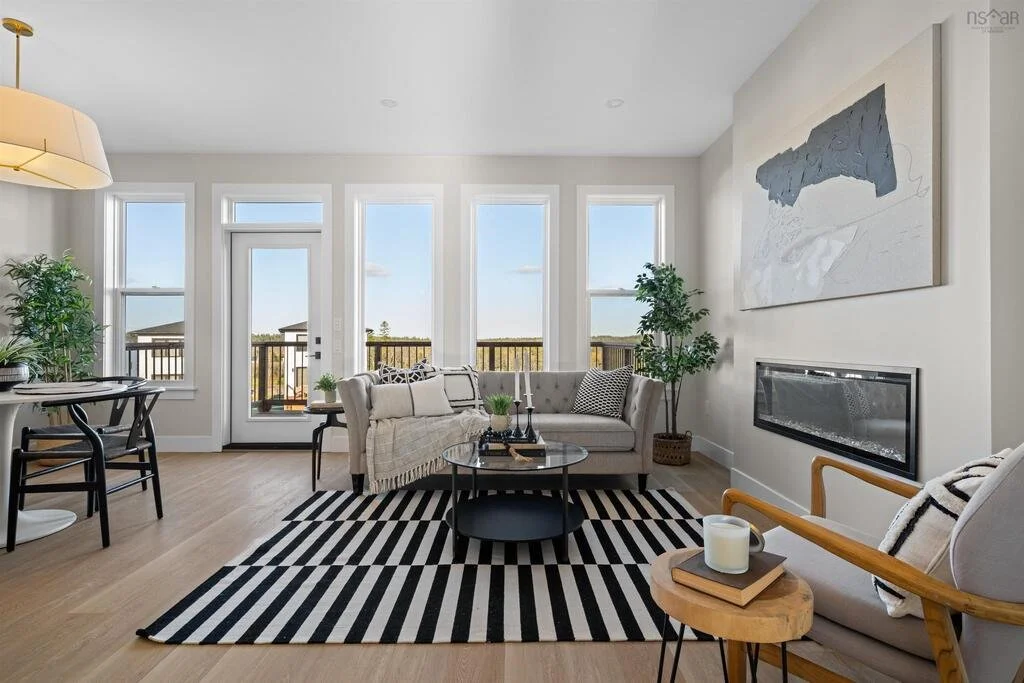 Bright living room with large windows, a beige sofa, striped black and white rug, modern black coffee table, and a wall-mounted fireplace.