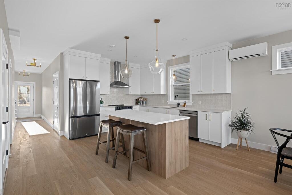 Kitchen with white cabinets, stainless steel refrigerator, island with wooden sides, pendant lights, and light wood flooring.