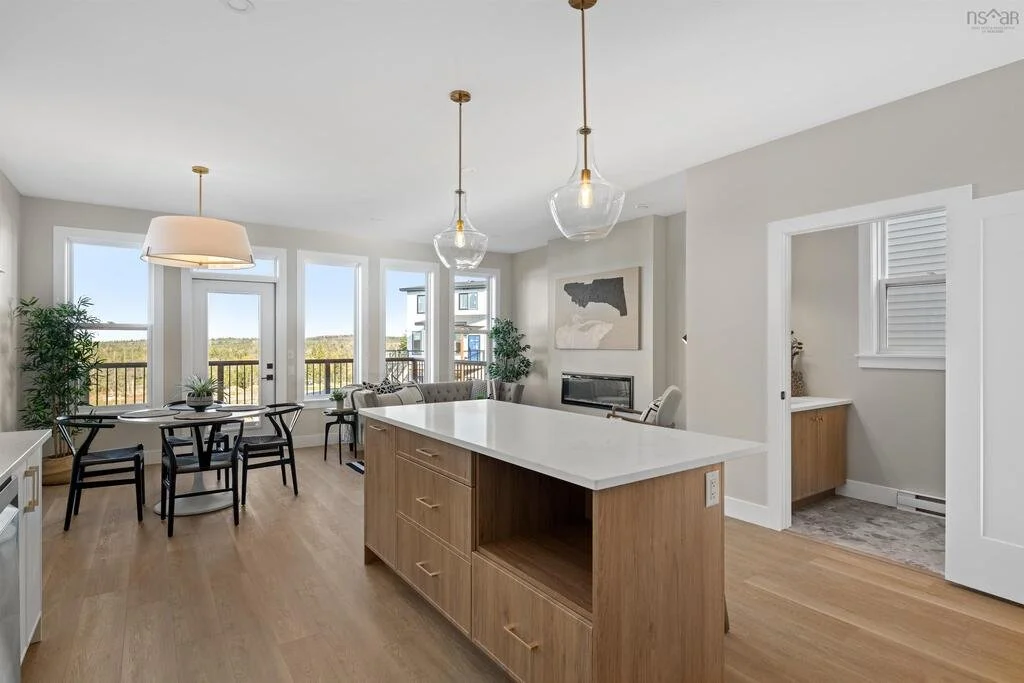 Open-concept living room and kitchen area with large windows, a round dining table with chairs, a sofa, a fireplace, and pendant lights.